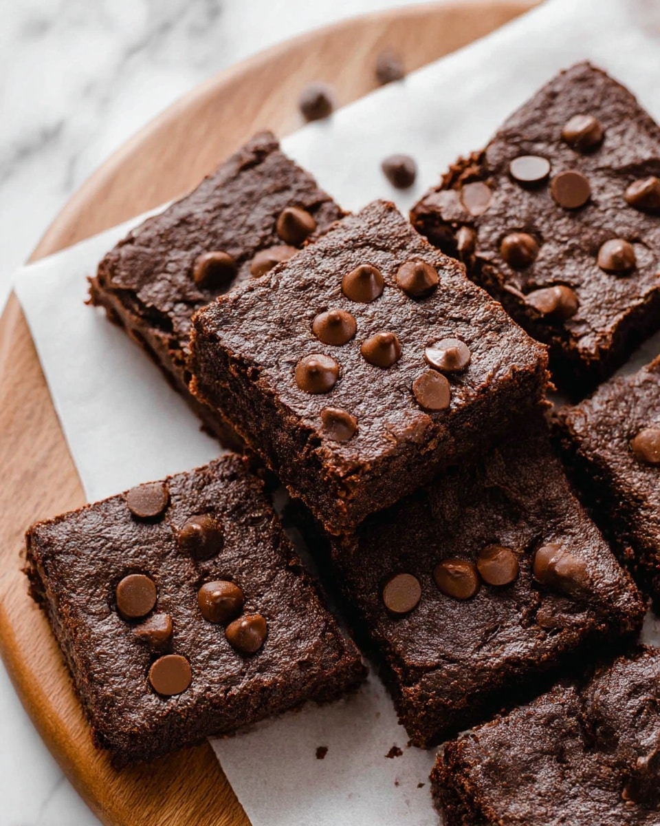 The image shows a close-up of square chocolate brownies stacked on white parchment paper placed on a wooden round board. Each brownie piece has a rough, cracked dark brown top layer with a moist, dense texture underneath. The top layer is decorated with scattered milk chocolate chips that add a smooth, shiny texture. There is a small triangular piece of solid chocolate near the brownies. The background and surface show a white marbled texture. photo taken with an iphone --ar 4:5 --v 6.1