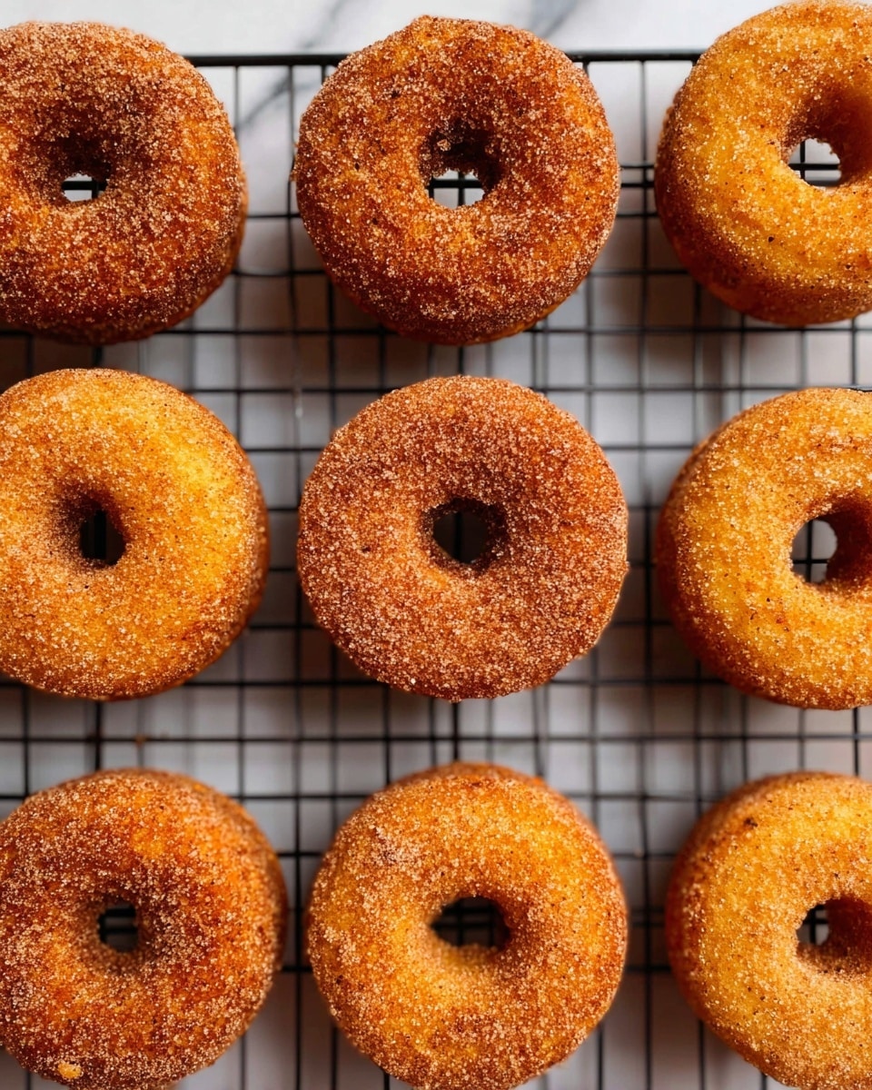 The image shows multiple cinnamon sugar donuts arranged in a grid pattern on a black cooling rack, placed over a white marbled surface. Each donut is golden brown with a rough texture due to the sugar and cinnamon coating. The donuts have a round shape with a hole in the middle, and the sugar granules give them a slightly sparkling appearance. The black rack contrasts with the warm tones of the donuts, making them look fresh and ready to eat. photo taken with an iphone --ar 4:5 --v 7