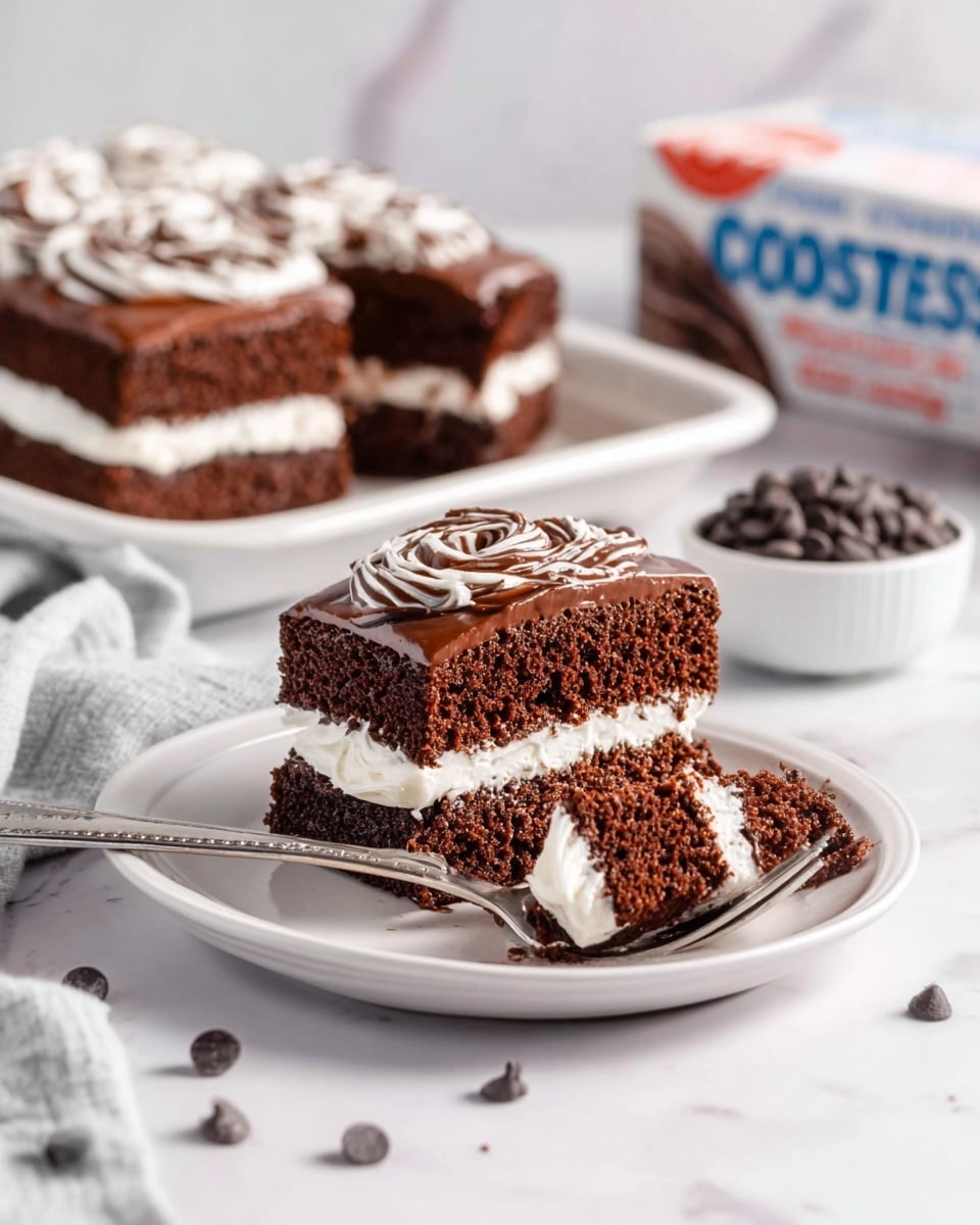 A close-up of a small white plate with a chocolate cake cut into two layers, separated by a thick white creamy filling. The top layer is decorated with a smooth chocolate frosting and white swirl icing. In front of the cake, a fork holds a small bite showing the soft texture of the chocolate cake and creamy middle. In the background, there is a white tray with more pieces of the same chocolate cake stacked in two layers with white filling, a small white bowl filled with dark chocolate chips, and a box showing the cake's packaging. Everything is set on a white marbled surface with soft lighting. Photo taken with an iphone --ar 4:5 --v 6.1
