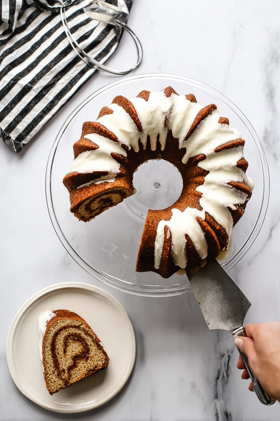 Cinnamon Bundt Cake, cinnamon bundt cake recipe, easy cinnamon cake, cozy cinnamon dessert, moist cinnamon loaf - A bundt cake with a rich brown color and a thick white icing drizzled over the top that flows down the sides, leaving some of the cake visible between the icing sections. The cake is placed on a clear glass pedestal plate on a white marbled surface. One slice is cut out and placed on a white plate nearby, showing a swirl pattern inside with light and dark brown layers. A woman's hand is holding the cake server that has been used to lift the slice from the bundt cake. There is a striped black and white napkin to the side with a metal cake server on it. photo taken with an iphone --ar 2:3 --v 7