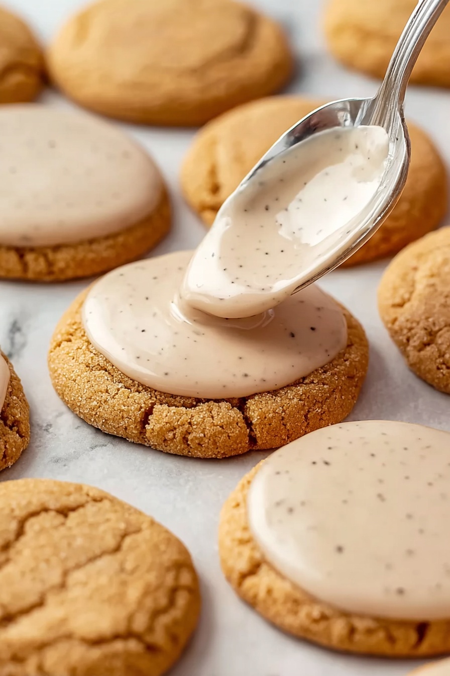 Brown Sugar Pop Tart Cookies, brown sugar cookies with cinnamon filling, homemade pop tart cookie recipe, chewy cinnamon cookies, easy dessert recipes - Round light brown cookies with a soft, cracked surface are arranged on a white marbled background. A silver spoon is shown spreading a smooth, pale beige icing with small dark specks on the top surface of one cookie near the center. Several other cookies already have the same thin layer of icing evenly covering their tops while some remain plain. The cookies are placed closely together in rows and the icing appears glossy and creamy. Photo taken with an iphone --ar 2:3 --v 7