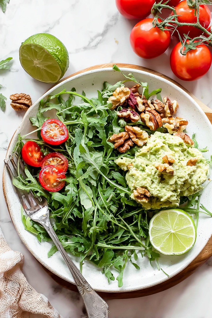 Healthy Greek Yogurt Avocado Chicken Salad, healthy chicken salad, avocado chicken recipe, Greek yogurt salad, keto friendly chicken salad - A white plate filled with a fresh salad on a white marbled surface. The bottom layer is a bed of dark green arugula leaves spread across the plate. Scattered on top are bright red cherry tomato halves and small brown walnut pieces. On one side, a creamy pale green mashed avocado mix is placed in a mound with a few walnut pieces on it. Two lime wedges, one light green and one yellow-green, rest on the mashed avocado. A silver fork is placed on the left side of the plate, partially resting on the salad. Nearby, whole red tomatoes on the vine and a halved lime sit on the white marbled background. Photo taken with an iphone --ar 2:3 --v 7