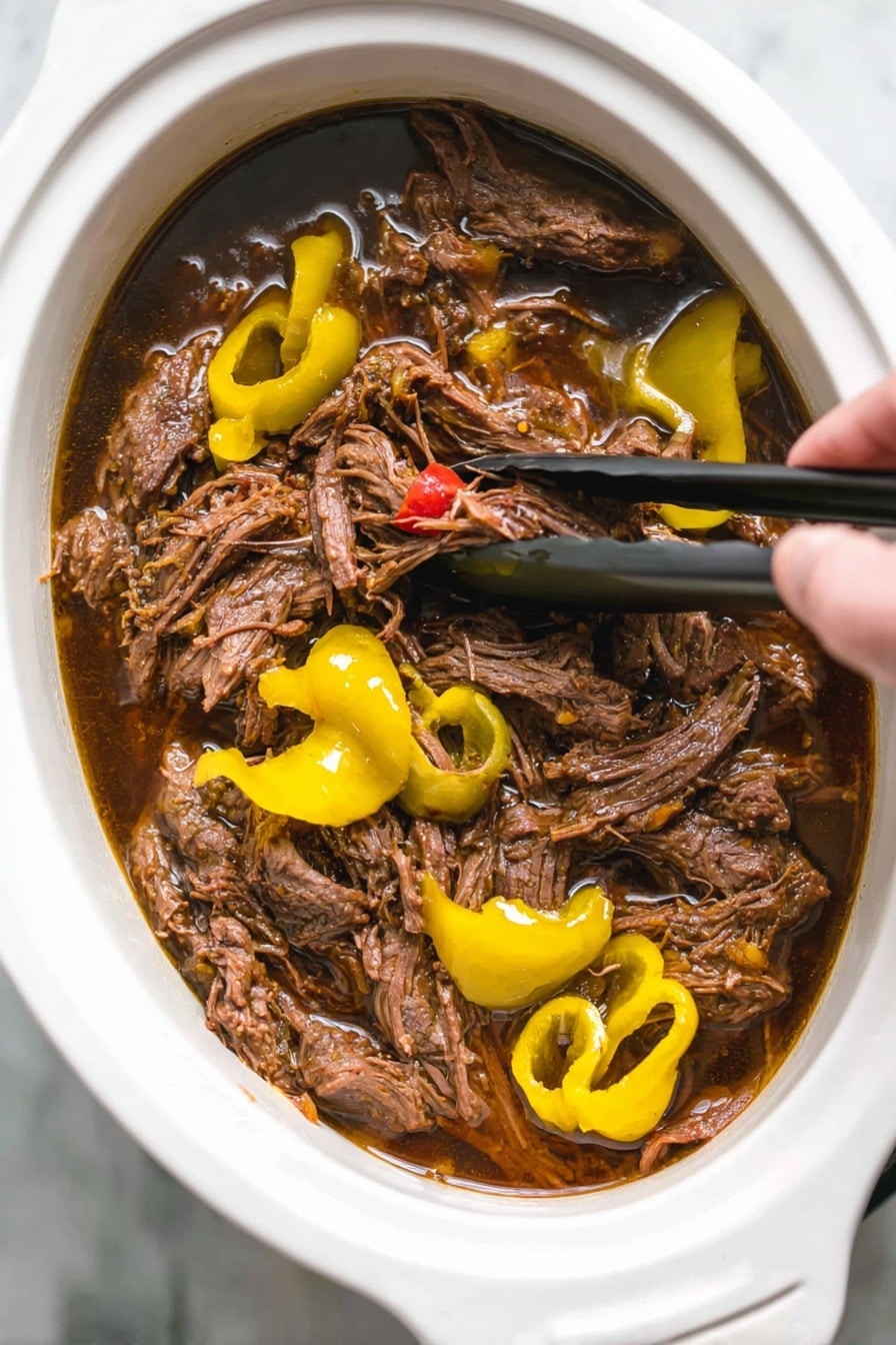 Italian Beef Sandwiches with Pepperoncini and Melted Cheese, Italian Beef Sandwich, Pepperoncini Beef Sandwich, Slow Cooker Italian Sandwich, Beef Sandwiches with Pepperoncini - A close-up shot of shredded brown meat soaked in dark brown juices inside a white oval slow cooker. The meat is mixed with bright yellow sliced peppers and whole pepper shapes on top. Woman's hand is visible holding black tongs, lifting some meat from the cooker. The background surface is white marble. photo taken with an iphone --ar 2:3 --v 7