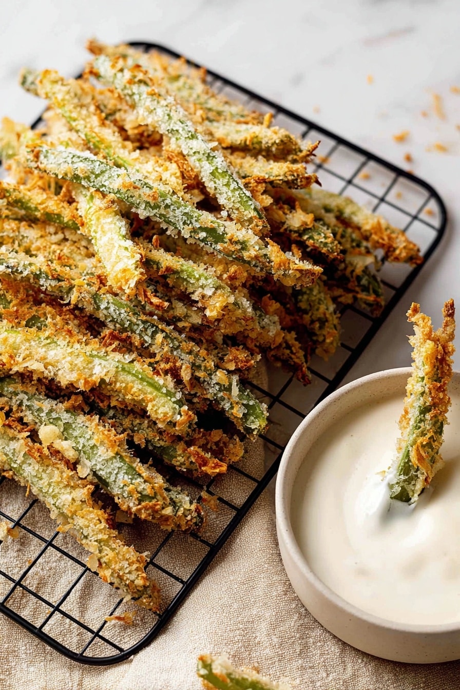 Green Bean Fries, crispy green bean sticks, healthy vegetable snacks, baked veggie fries, easy appetizer recipes - The image shows many breaded green beans stacked on a black wire cooling rack on a white marbled surface with a beige cloth underneath. The beans have a crunchy, golden-brown coating with bits of light and darker browns and the green of the beans is visible under the crumbs. To the right, there is a white bowl filled with thick, creamy white dip, with two breaded green beans dipped into it. The texture of the dip is smooth and slightly shiny. Photo taken with an iphone --ar 2:3 --v 7