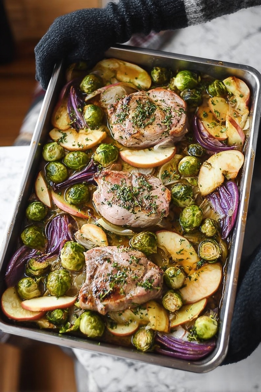 Sheet Pan Pork Chop Supper with Apple, Brussels Sprouts, and Sage, pork chop sheet pan dinner, easy pork chop recipes, cozy weeknight meals, apple and Brussels sprouts pork - A metal baking tray with four large light pink pork pieces in the center, sprinkled with green herbs, surrounded by bright green halved Brussels sprouts and wedges of purple-red onion and golden brown apple slices, all on a white marbled surface. Steam rises from the tray, held by a woman’s hand wearing a black glove on the left side. The vegetables and pork look roasted with some browned edges. photo taken with an iphone --ar 2:3 --v 7