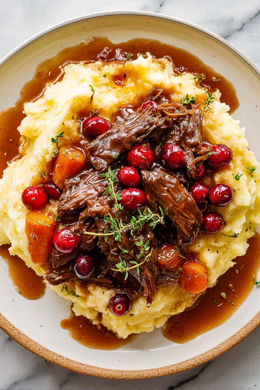 Cranberry Balsamic Roast Beef, cranberry balsamic sauce, slow roast beef recipes, holiday beef main dish, savory beef dinner ideas - A white plate holds a large bed of soft, creamy mashed potatoes that have a smooth, slightly lumpy texture and a pale yellow color. On top, there are several pieces of dark brown shredded beef covered in a glossy, thick brown gravy with visible chunks of carrots, pearl onions, and whole bright red cranberries scattered throughout. Fresh small green herb leaves, possibly thyme, are sprinkled over the dish. Some gravy has spilled onto the plate, adding a rich shine. The plate sits on a white marbled surface. Photo taken with an iphone --ar 2:3 --v 7
