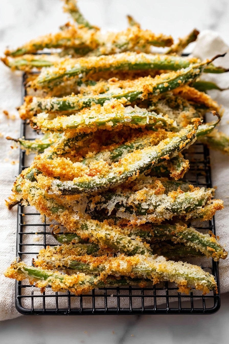 Green Bean Fries, crispy green bean sticks, healthy vegetable snacks, baked veggie fries, easy appetizer recipes - The image shows a stack of crispy baked green beans coated with a light golden-brown breadcrumb crust. The green beans are arranged in a slightly overlapping pile on a black wire rack that sits on top of a white marbled surface with a soft white cloth underneath. The crumb coating is uneven with some areas showing more toasted crispiness and a mix of pale and deeper golden colors. The green beans are long and thin, with their stems visible at the edges, and the texture looks crunchy and rustic. photo taken with an iphone --ar 2:3 --v 7