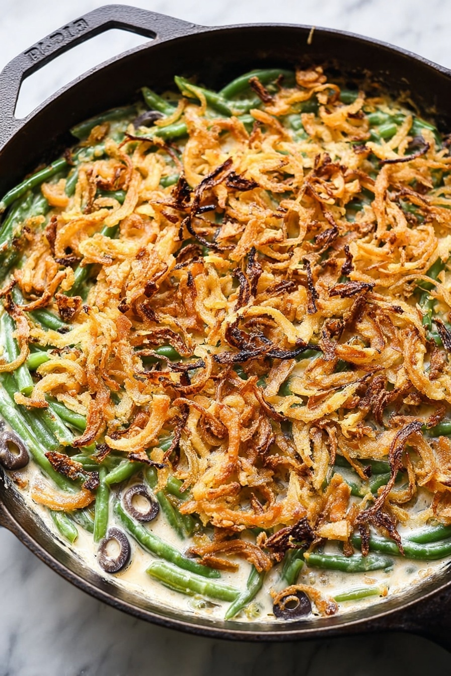 Vegan Green Bean Casserole, vegan green bean casserole without dairy, plant-based green bean casserole, healthy vegan side dish, holiday vegan casserole - This image shows a close-up of a baked green bean casserole in a cast iron pan placed on a white marbled surface. The bottom layer consists of bright green beans mixed with sliced black olives visible within a creamy, white sauce. On top of this, there is a thick, even layer of crispy, golden-brown fried onion strips spread across the entire pan, giving the dish texture and a crunchy appearance. Some onion strips have darker, almost burnt edges which add color contrast. The round pan's black handle is partly visible, framing the dish. Photo taken with an iphone --ar 2:3 --v 7