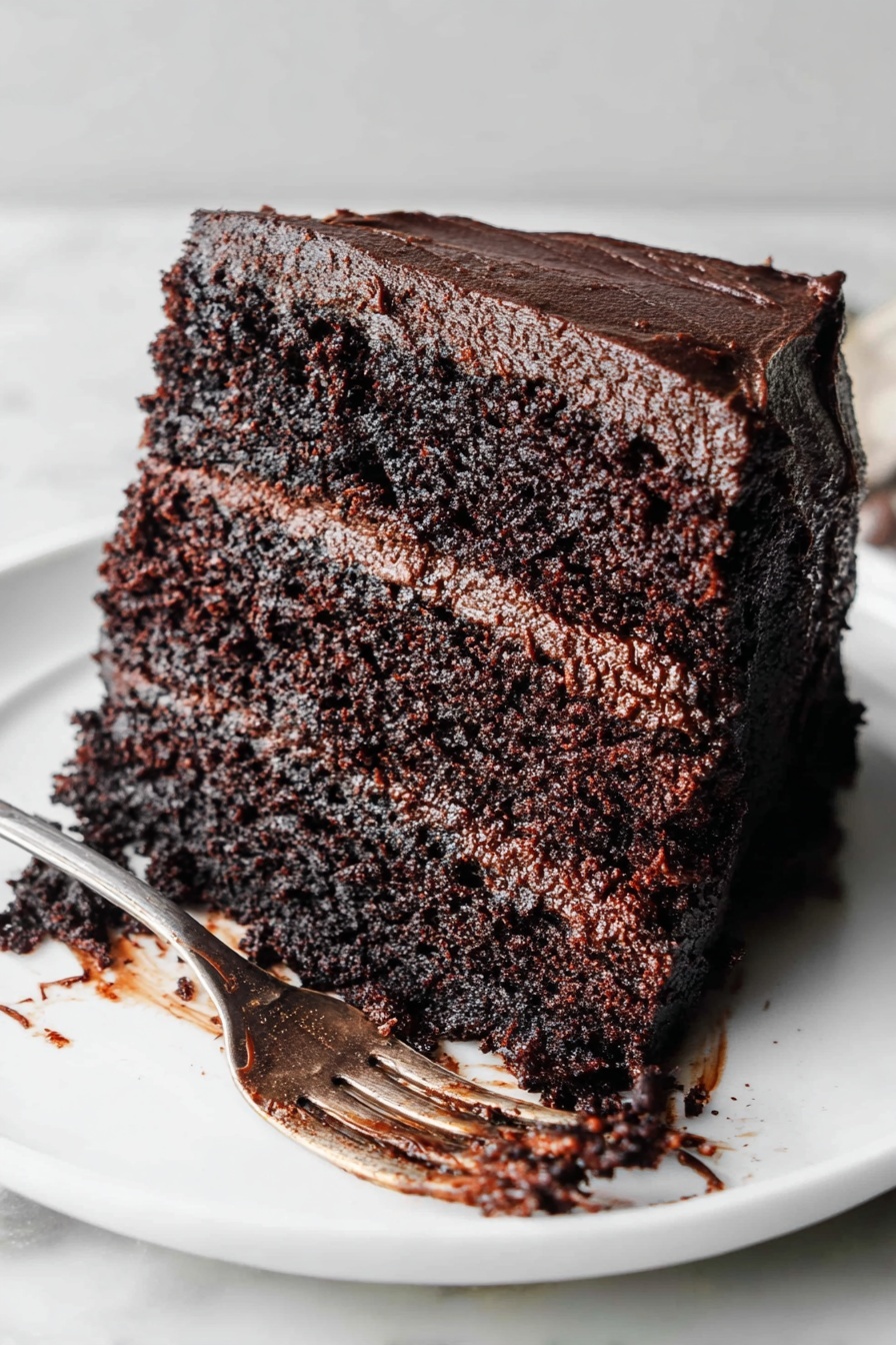 The Most Amazing Chocolate Cake, best chocolate cake, moist chocolate cake, chocolate cake recipe from scratch, rich chocolate cake - A thick slice of three-layer dark chocolate cake lies on a white plate with a white marbled background. Each cake layer is moist and spongy, with rich dark brown color and tiny air holes visible throughout. Between and covering the top and sides is a smooth, thick layer of dark chocolate frosting with a glossy texture. Chocolate crumbs and a bit of frosting stick to a silver fork resting next to the cake slice. Photo taken with an iphone --ar 2:3 --v 7