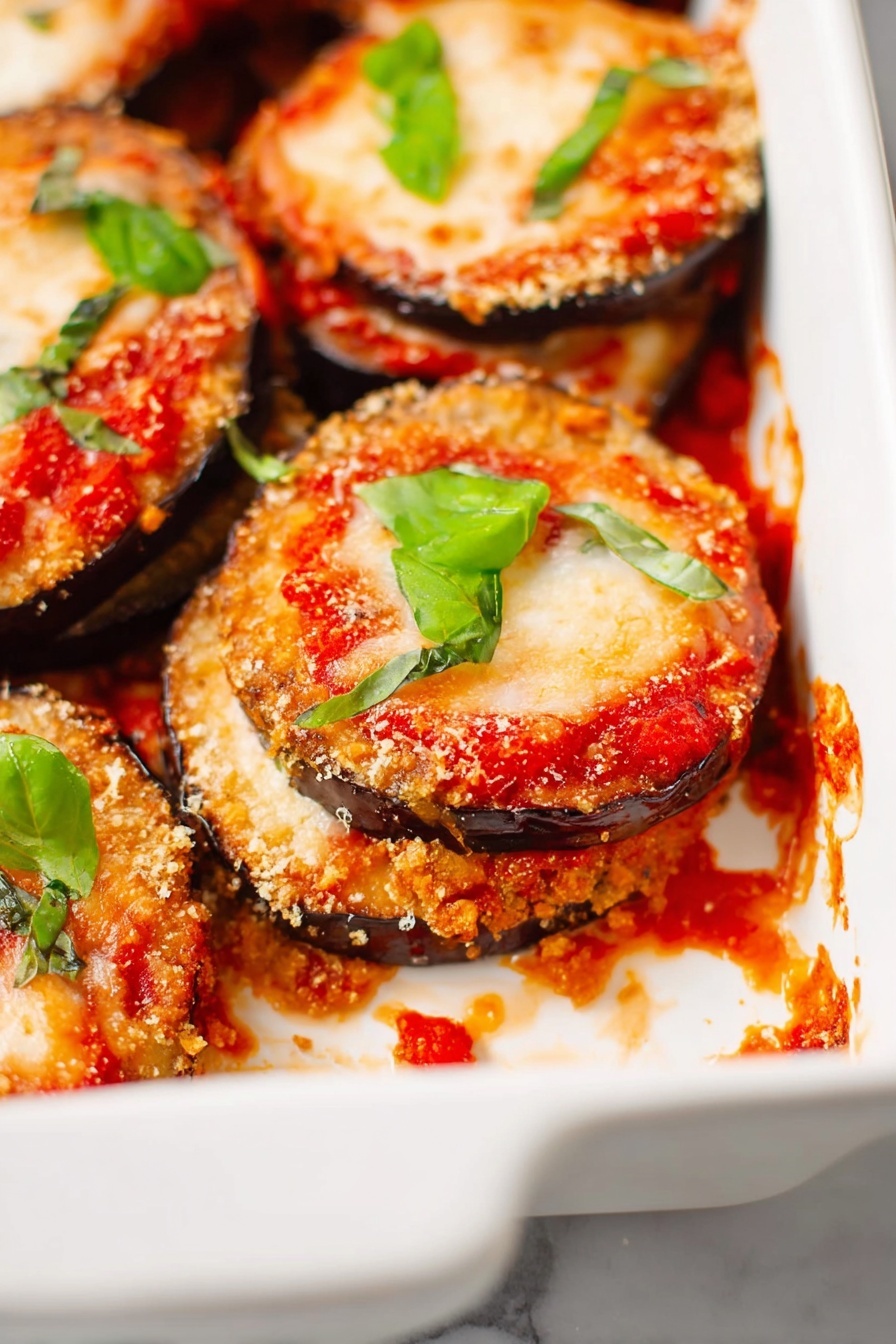 Vegan Eggplant Parmesan, vegan eggplant parm recipe, plant-based eggplant parmesan, vegan Italian dinner, healthy eggplant recipes - The image shows a white ceramic baking dish filled with several layered stacks of eggplant Parmesan. Each stack has a bottom layer of crispy, golden-brown eggplant slices with a rough texture, topped with rich red tomato sauce, then a layer of melted pale orange cheese that is slightly bubbly and browned in spots. Bright green basil leaves are scattered on top of the stacks and around the dish for color contrast. There are some tomato sauce spills and melted cheese crumbs inside the dish on a white marbled surface. Photo taken with an iphone --ar 2:3 --v 7