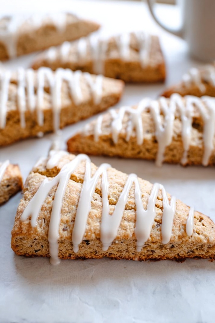 Cinnamon Vanilla Biscotti, biscotti recipe, homemade biscotti, coffee pairing cookies, crunchy vanilla biscotti - This image shows several triangular slices of light brown scones arranged on white parchment paper over a white marbled surface. Each scone slice has a visible crumbly texture with small dark specks inside. On top of each slice, there is a thick white icing drizzle applied in vertical lines, adding contrast and a smooth, glossy look to the rough texture of the scones. The focus is on a front scone slice, with others blurred in the background, giving depth to the image. photo taken with an iphone --ar 2:3 --v 7