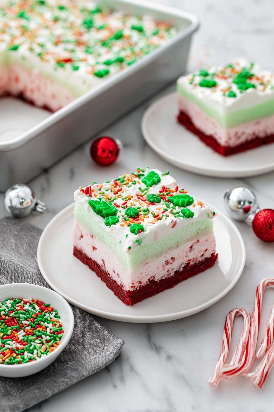 Christmas Red Velvet Lasagna Dessert, festive red velvet layered dessert, holiday red velvet lasagna, Christmas dessert ideas, easy holiday layered dessert - The image shows a festive layered dessert square on a white plate, placed on a white marbled surface. The dessert has four distinct layers: the bottom layer is a dense dark red cake, followed by a light pink creamy layer with red specks, then a smooth pale green gelatin layer, and finally topped with a thick white whipped cream layer decorated with green, red, orange, and white sprinkles shaped like leaves, dots, and sticks. In the background, there is a silver baking pan with a large portion of the same dessert topped with sprinkles, and another smaller white plate holds a similarly decorated dessert square. Nearby, a small white bowl filled with matching festive green and red sprinkles sits next to two small candy canes, a silver ornament ball, a red ornament ball, and a gray cloth napkin. Photo taken with an iphone --ar 2:3 --v 7
