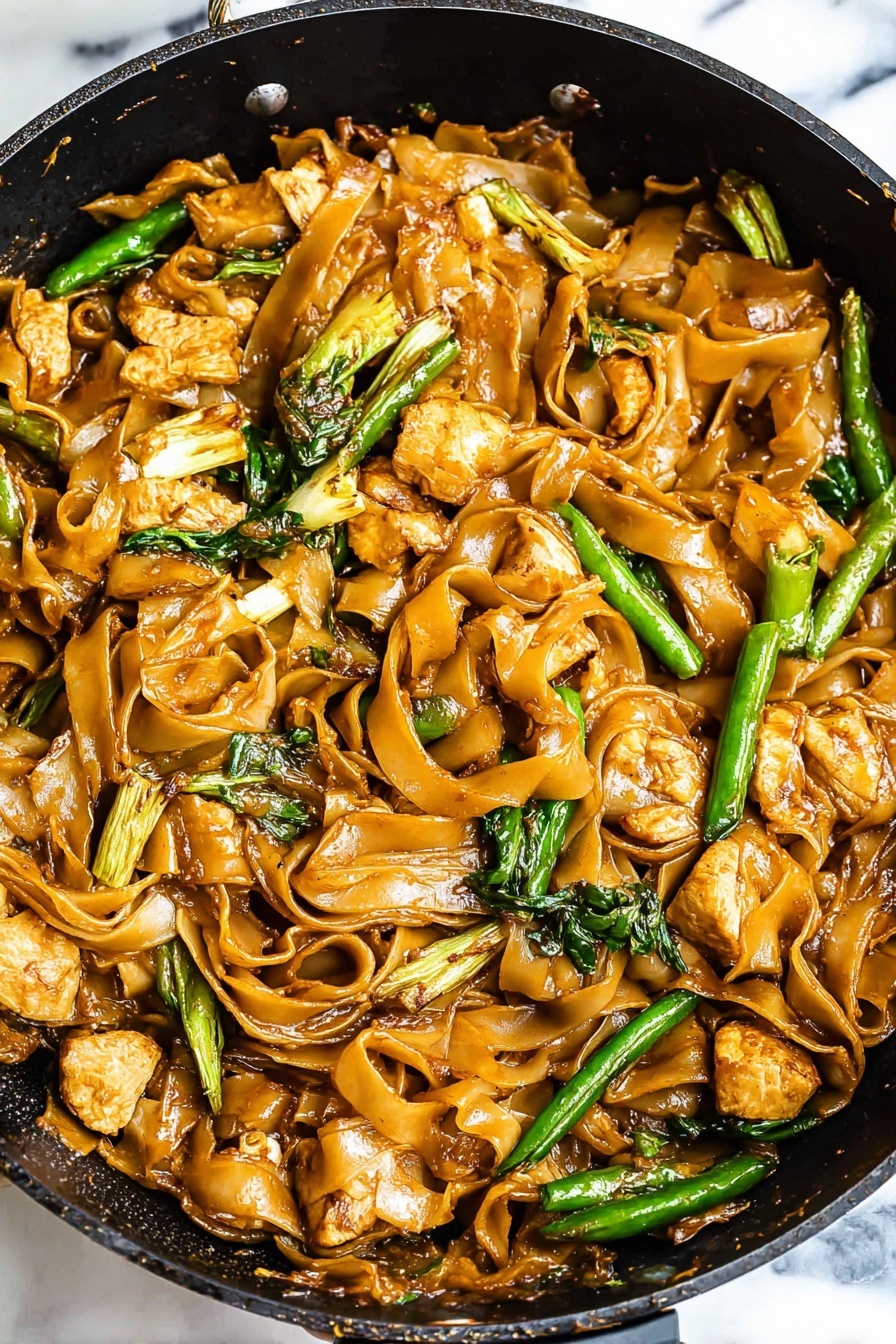 15 Minute Thai Pad See Ew Stir Fry, Thai stir fry recipes, quick Thai dinner ideas, authentic Pad See Ew, easy Thai noodle recipes - The image shows a pan filled with a stir-fry dish that has several layers and textures. The bottom layer is made of wide, flat noodles cooked to a soft, shiny brown color from the sauce. Mixed throughout the noodles are medium-sized chunks of light brown cooked chicken pieces with slight browning on their edges. Scattered on top and throughout are bright green leafy vegetables and long green beans, adding a fresh look. The sauce gives everything a glossy, slightly oily texture, highlighting the folds and curls of the noodles. The pan is black inside with a white marbled surface underneath it visible at the edges. Photo taken with an iphone --ar 2:3 --v 7