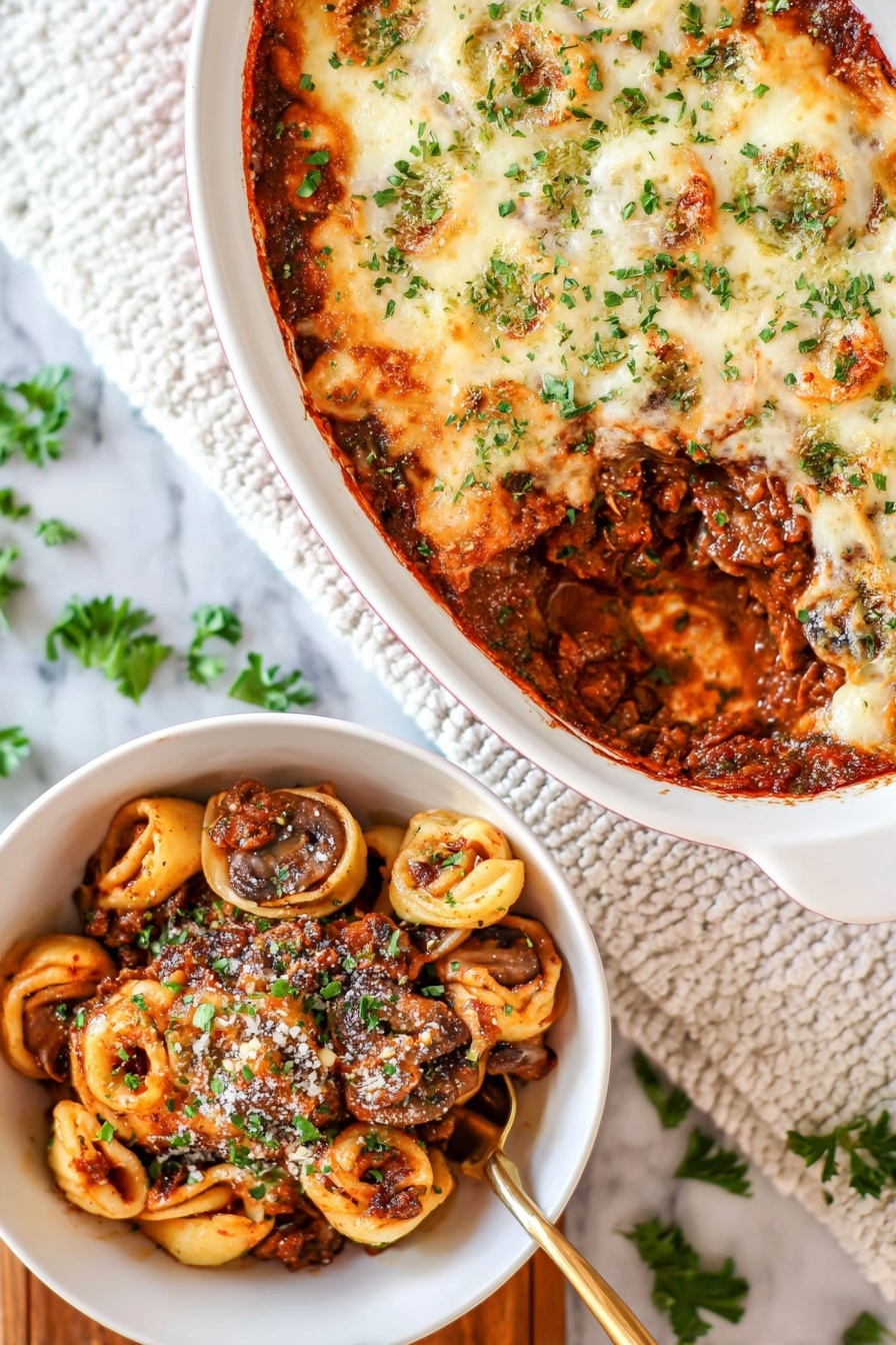 Cheesy Baked Tortellini with Beef, baked tortellini with beef, cheesy pasta bake, hearty meat tortellini casserole, comforting baked tortellini recipe - The image shows a white oval baking dish with a layered casserole on a white marbled surface. The top layer is melted, lightly browned cheese sprinkled with green herbs. A section is scooped out, revealing a rich, dark brown meat sauce mixed with whole mushrooms and tortillas shaped like small circles inside the dish. Next to it is a white bowl filled with a serving of the casserole, showing layers of browned meat sauce, mushrooms, and pasta circles, all topped with some grated cheese and chopped green herbs. A golden spoon is partially visible in the bowl. The background includes a white textured cloth and scattered green herb leaves. photo taken with an iphone --ar 2:3 --v 7