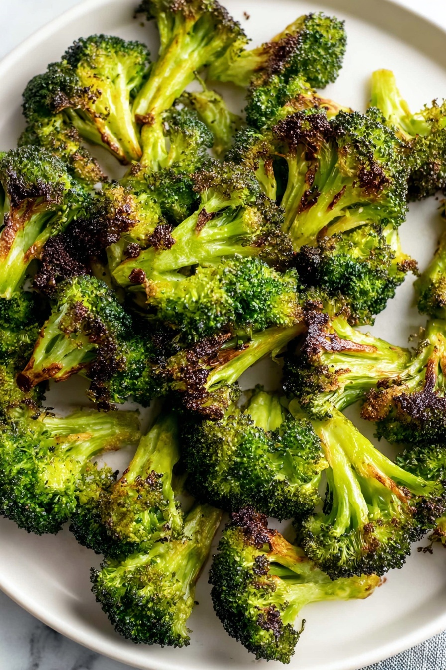 Oven Roasted Broccoli with Garlic and Paprika, roasted broccoli recipes, healthy roasted broccoli, garlic broccoli side dish, smoky broccoli roasted - A white round plate is filled with many pieces of roasted broccoli. Each broccoli piece shows a bright green color with dark brown, crispy edges where it is roasted. The broccoli is scattered all over the plate, with some pieces standing up and others lying flat, showing their textured tops and thick stalks. The plate is placed on a white marbled surface. photo taken with an iphone --ar 2:3 --v 7