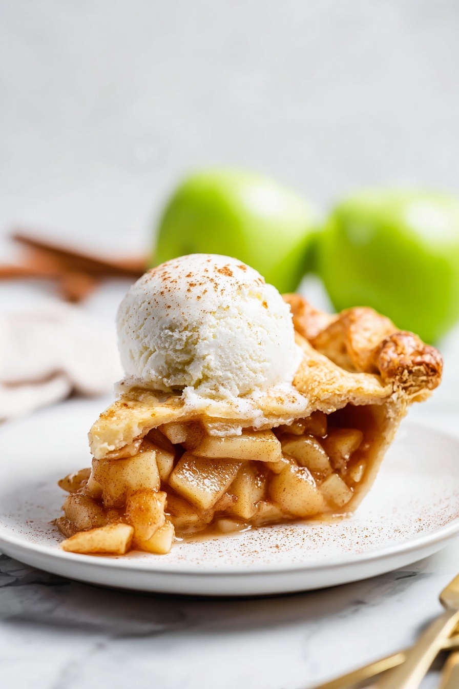 Vegan Pear Pie with Chai Spices, vegan pear pie, chai spice dessert, vegan fruit pie, healthy vegan dessert - A slice of apple pie sits on a white plate, showing three main layers: the bottom crust is golden brown and slightly flaky, the middle layer is filled with soft, cinnamon-spiced apple pieces that look juicy and tender, and the top crust is also golden with a slight sprinkle of sugar. On top of the pie slice is a round scoop of white ice cream with a light dusting of cinnamon. The plate rests on a white marbled surface, and in the background, out of focus, two green apples and a fork and knife are visible. Photo taken with an iphone --ar 2:3 --v 7