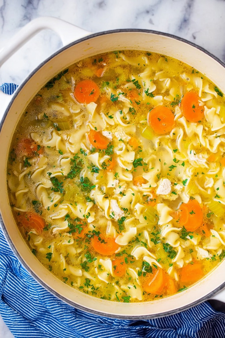 Vegan Chicken Noodle Soup, vegan soup recipe, plant-based chicken noodle soup, healthy vegan soup, comforting vegan noodle soup - A white pot filled with clear yellow broth soup containing wavy egg noodles that float through the liquid. Slices of bright orange carrots and pale green celery are mixed evenly throughout the soup, along with small pieces of white chicken. The soup is topped with finely chopped fresh green herbs, adding small bursts of color. The pot is resting on a white marbled surface next to a blue striped cloth. Photo taken with an iphone --ar 2:3 --v 7