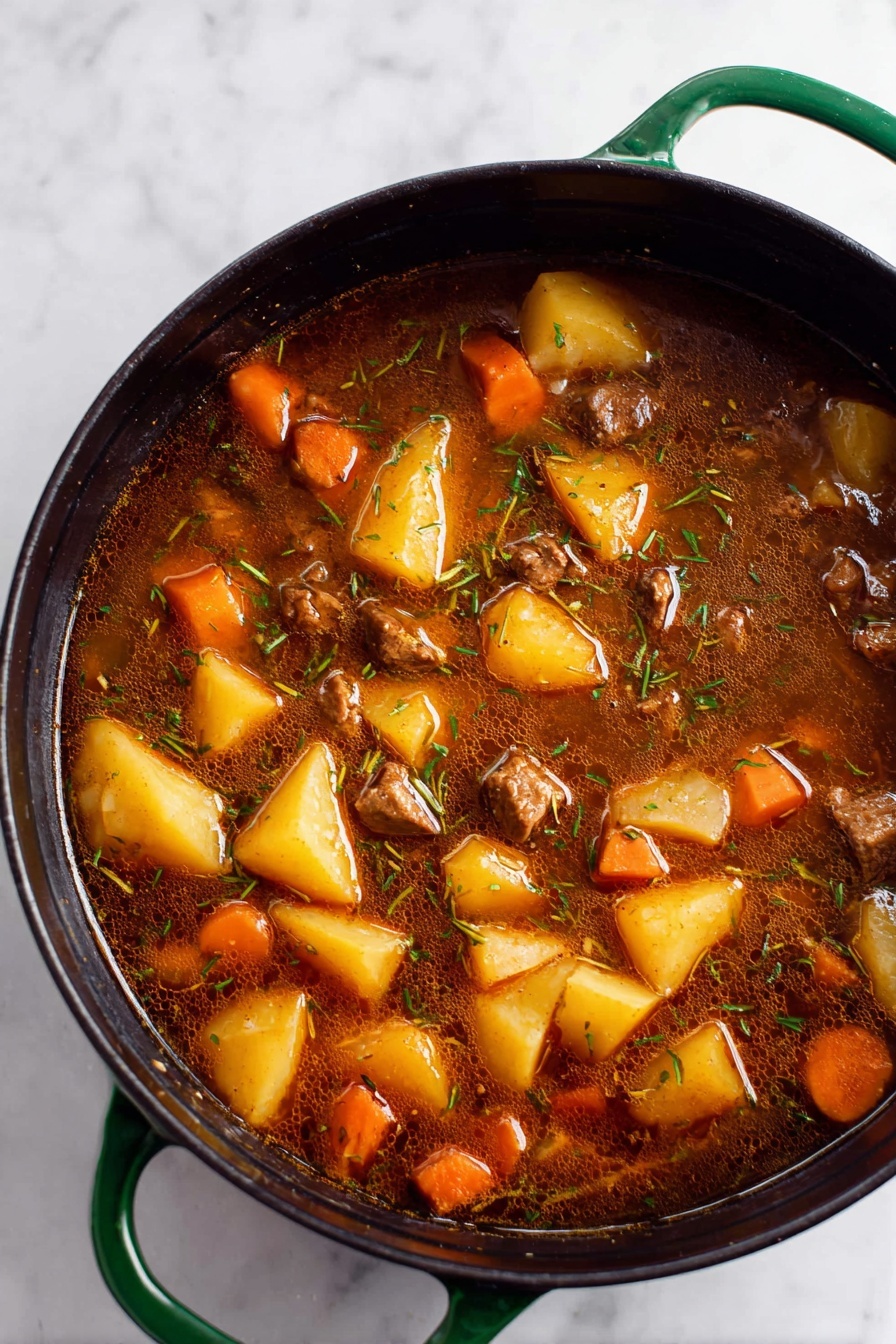 Vegan Irish Stew with Beer and Vegetables, hearty plant-based stew, vegan Irish stew recipe, vegan beer vegetable stew, plant-based Irish stew - A close-up top view of a large black pot with green handles filled with a rich brown stew. The stew has large chunks of yellow potatoes, orange carrot pieces, and small cubes of brown meat mixed evenly throughout. The broth is dark, slightly oily, with visible thin strands of herbs floating on the surface. The pot sits on a white marbled surface. photo taken with an iphone --ar 2:3 --v 7