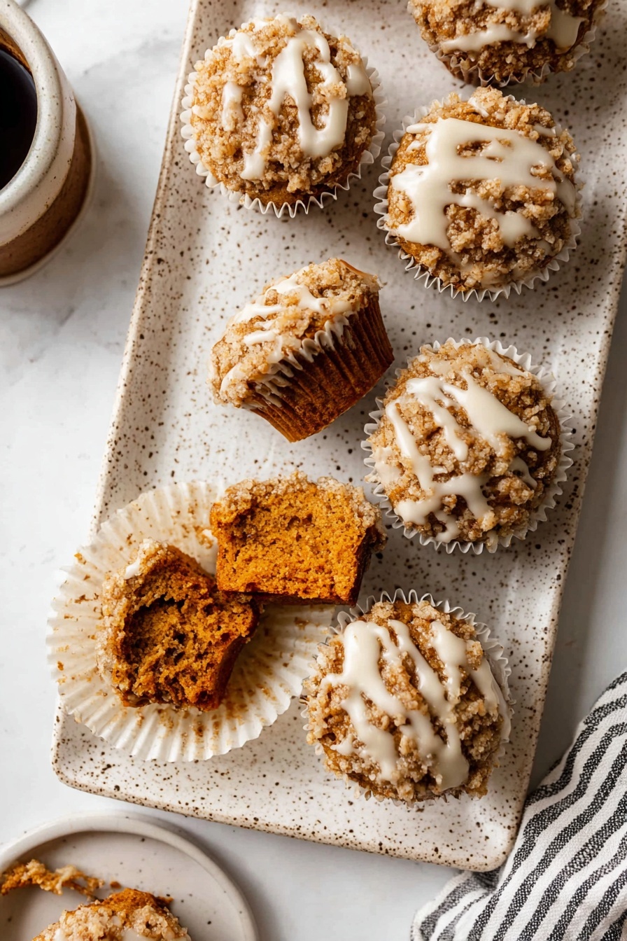Pumpkin Crumb Muffins, Fall Pumpkin Muffins, Pumpkin Muffin Recipe, Easy Pumpkin Muffins, Cinnamon Pumpkin Muffins - The image shows a white speckled rectangular plate holding seven small muffins with crumbly tops. Each muffin has a rough, light brown crumb layer with a drizzle of white icing over it. Two muffins in the front have bites taken out, showing a dense, dark orange interior. The muffins sit inside white paper liners arranged close to each other. The plate is on a white marbled textured surface with part of a cup of coffee and a striped cloth visible on the edges. photo taken with an iphone --ar 2:3 --v 7