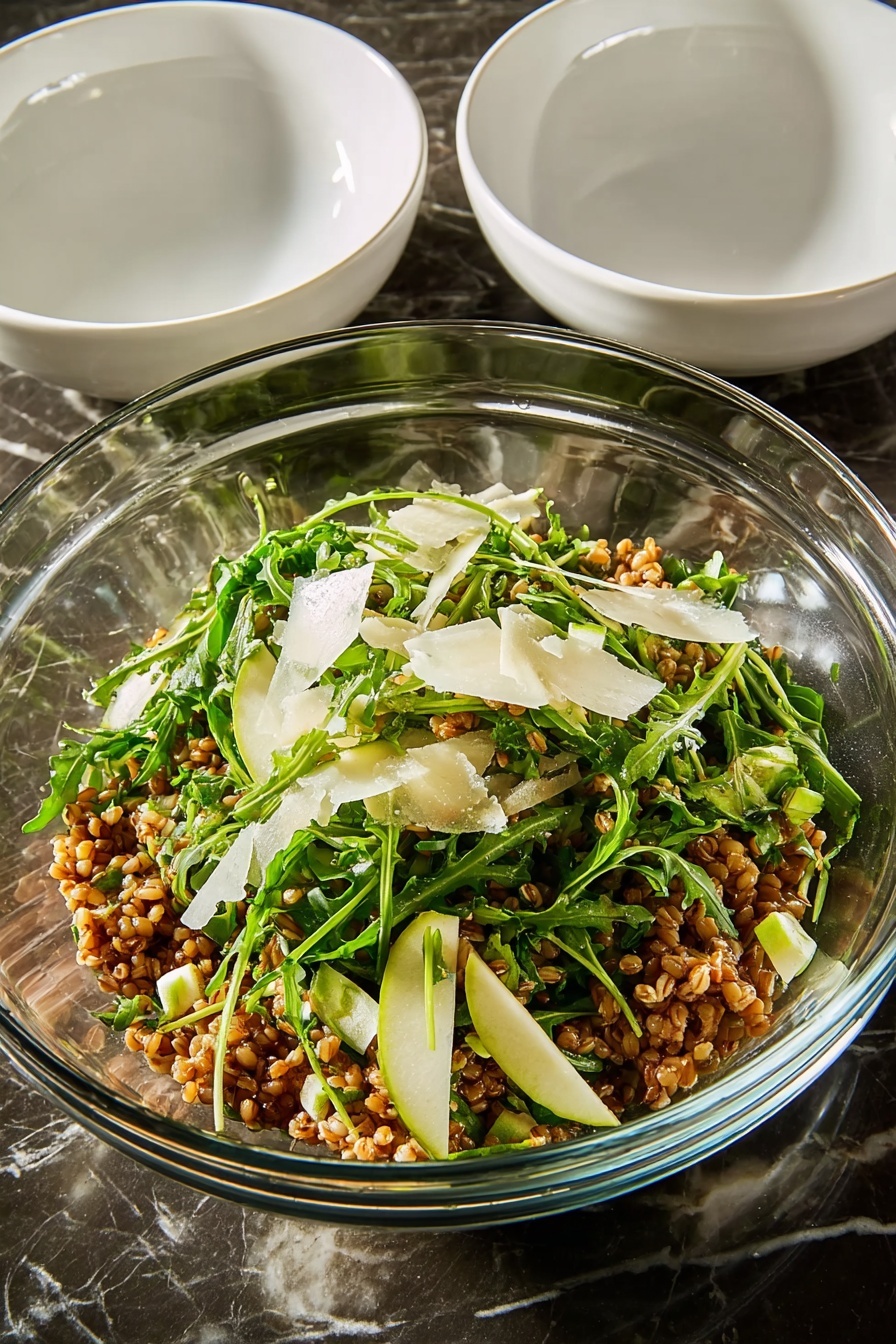 Healthy Farro Salad with Apple and Arugula, nutritious farro salad, fresh apple arugula salad, healthy grain salads, easy healthy salad recipes - A large white round plate filled with a mixed salad that has several layers visible: the base layer is light brown cooked grains, mixed evenly with bright green arugula leaves scattered throughout. There are small, light green diced pieces of zucchini layered on top, along with thin, slightly browned slices of caramelized onions that add texture. Sprinkled lightly over the salad are thin shavings of light-colored cheese and small pieces of green herbs, giving a fresh look. The salad shows a mix of textures from soft grains to leafy greens and crunchy bits, all placed on a white marbled surface. photo taken with an iphone --ar 2:3 --v 7