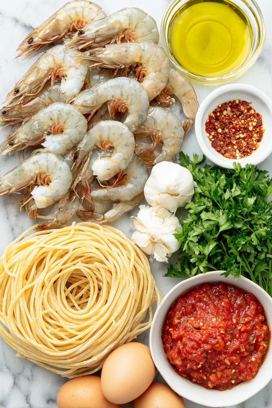 Shrimp Fra Diavolo Pasta, spicy shrimp pasta recipe, garlic shrimp pasta, quick seafood pasta, easy Italian pasta dishes - Flat lay of dry linguine pasta neatly coiled, plump large shrimp with tails on arranged in a gentle curve, a small white bowl filled with shiny olive oil, a small white bowl containing bright red Calabrian chili paste, a cluster of fresh garlic cloves with papery skins intact, a small white bowl of vivid red crushed San Marzano tomatoes, fresh vibrant green parsley sprigs artistically placed, a small white bowl holding mixed red pepper flakes, and three whole uncracked brown eggs arranged symmetrically, all placed on a clean white marble surface, soft natural light, photo taken with an iPhone, professional food photography style, fresh ingredients, white ceramic bowls, no bottles, no duplicates, no utensils, no packaging --ar 2:3 --v 7 --p m7354615311229779997