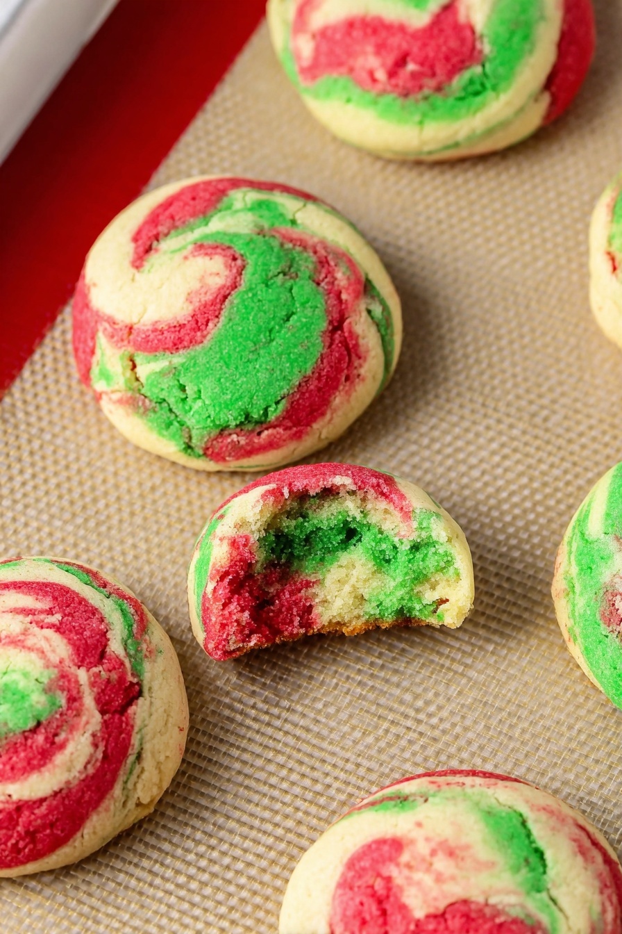 Christmas Peppermint Cheesecake Cookies, festive holiday cookies, peppermint cheesecake cookies, easy Christmas cookies, holiday baking recipes - This image shows a baking tray lined with a beige silicone mat that holds eight round cookie dough balls. Each ball has three swirled colors: green, red, and white, giving a marbled effect. The dough balls are spaced evenly, with a slightly rough texture on top and smooth sides. The tray has a silver metal edge and a red silicone border around the baking mat. The background is a white marbled texture. photo taken with an iphone --ar 2:3 --v 7