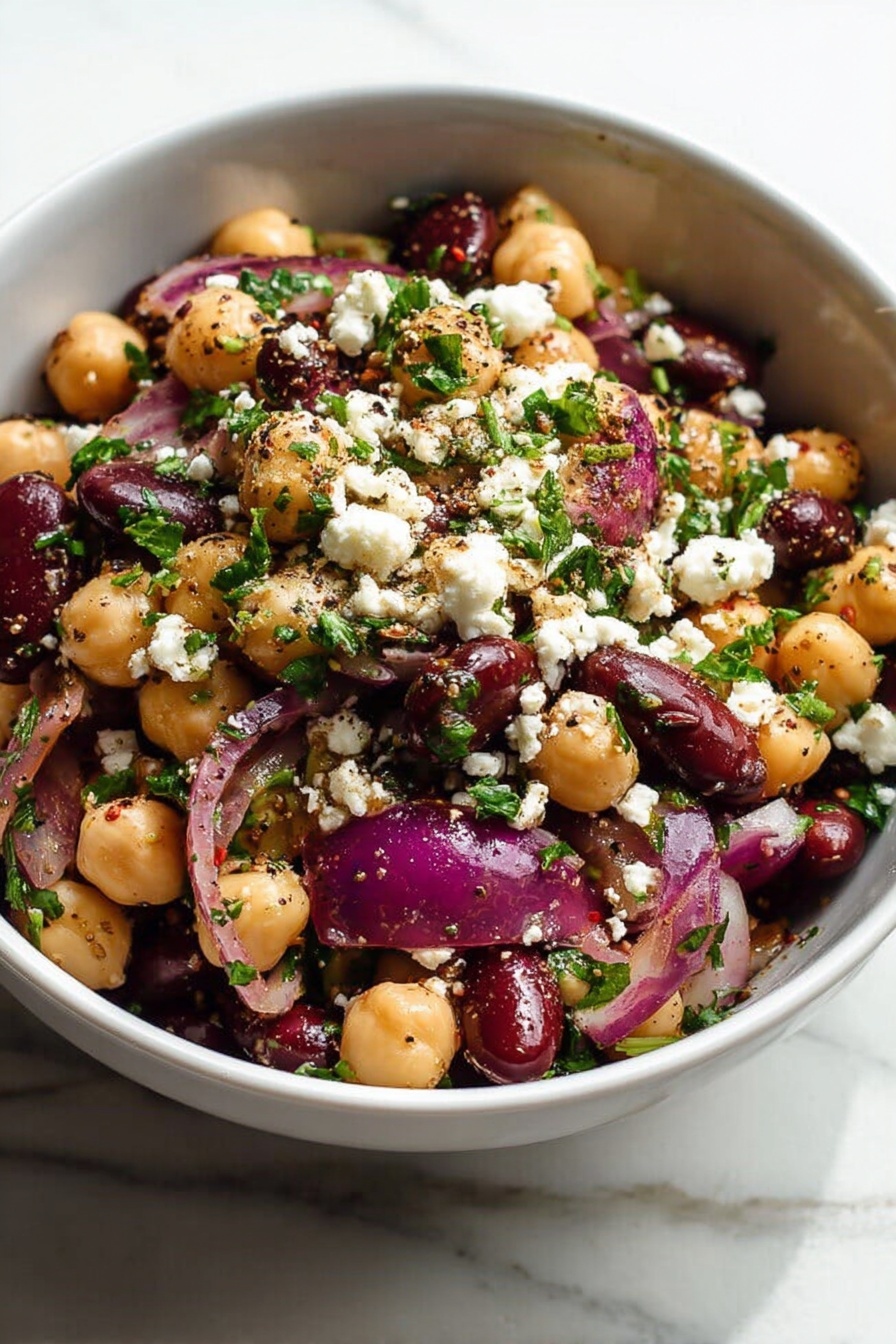 Chickpea and Black Bean Salad, Chickpea and Black Bean Salad Easy, Healthy Chickpea and Black Bean Salad, Vegetarian Bean Salad, Quick Vegetable Salad - A white bowl filled with a salad showing three main layers: the bottom layer is a mix of beige chickpeas and dark red kidney beans; the middle layer includes large pieces of purple-red onion; the top layer is sprinkled with white crumbled cheese and small bits of bright green parsley, all mixed with visible black pepper and seasoning specks. The salad looks fresh and colorful, sitting on a white marbled surface, photo taken with an iphone --ar 2:3 --v 7