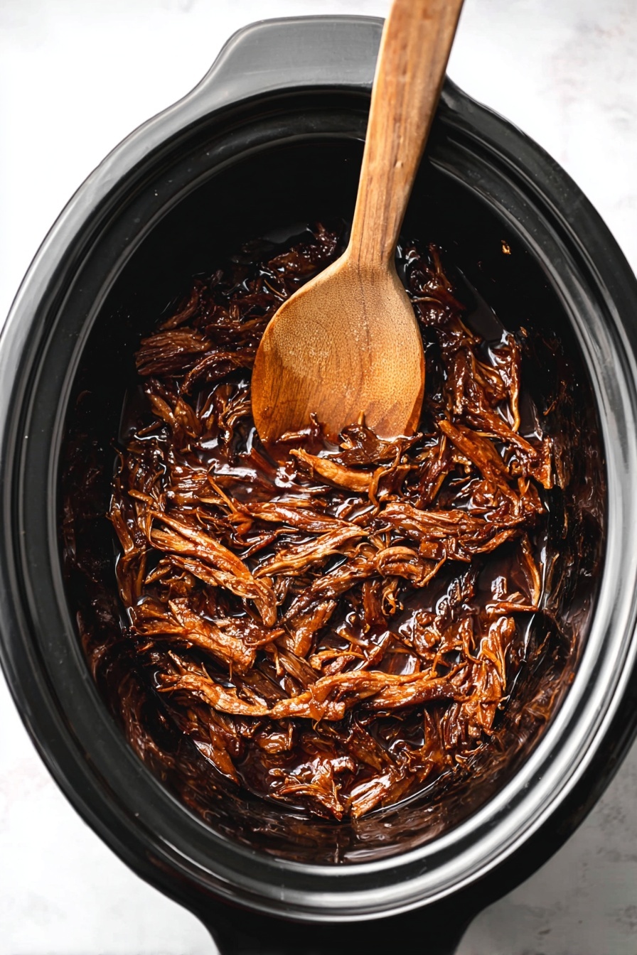 Slow Cooker Honey BBQ Beef Brisket, tender beef brisket, BBQ beef recipes, slow cooker beef dinner, easy BBQ brisket - Inside a black slow cooker, there is a single layer of dark brown shredded meat with a shiny, sticky sauce coating it. Resting partially on top of the meat is a wooden spoon with a smooth brown texture. The slow cooker sits on a white marbled surface. photo taken with an iphone --ar 2:3 --v 7