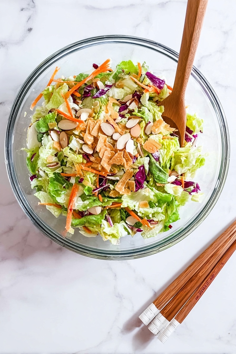 Asian Crunch Chicken Salad with Crispy Egg Roll Bases, Asian chicken salad, crispy egg roll salad, healthy Asian chicken salad, flavorful Asian salad - A clear glass bowl sits on a white marbled surface, filled with a colorful salad made of several layers: the bottom layer has bright green lettuce leaves mixed with light green cabbage, scattered on top are thin orange carrot strips and bits of purple cabbage, then sprinkled with light brown almond slices and thin crispy golden strips, creating a fresh and crunchy look. Beside the bowl, a pair of wooden chopsticks with white tips rests on the surface. photo taken with an iphone --ar 2:3 --v 7