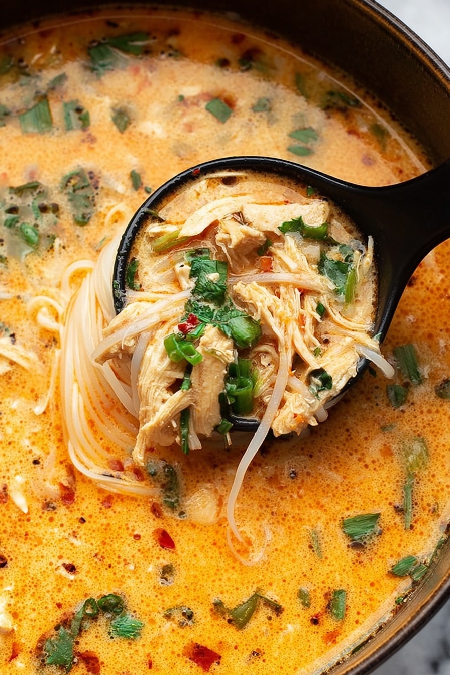 Thai Chicken Curry Soup, Thai Chicken Curry, Easy Thai Soup, Coconut Curry Soup, Spicy Thai Soup - The image shows a close-up of a creamy orange soup with thin white noodles and small pieces of shredded light brown chicken. The soup is garnished with bright green chopped herbs, mostly cilantro and green onions, floating on top. A black ladle holds a scoop of noodles and chicken, partially lifted from the soup. The surface of the soup looks smooth with some specks of black pepper and red chili flakes. The background is a white marbled texture. photo taken with an iphone --ar 2:3 --v 7