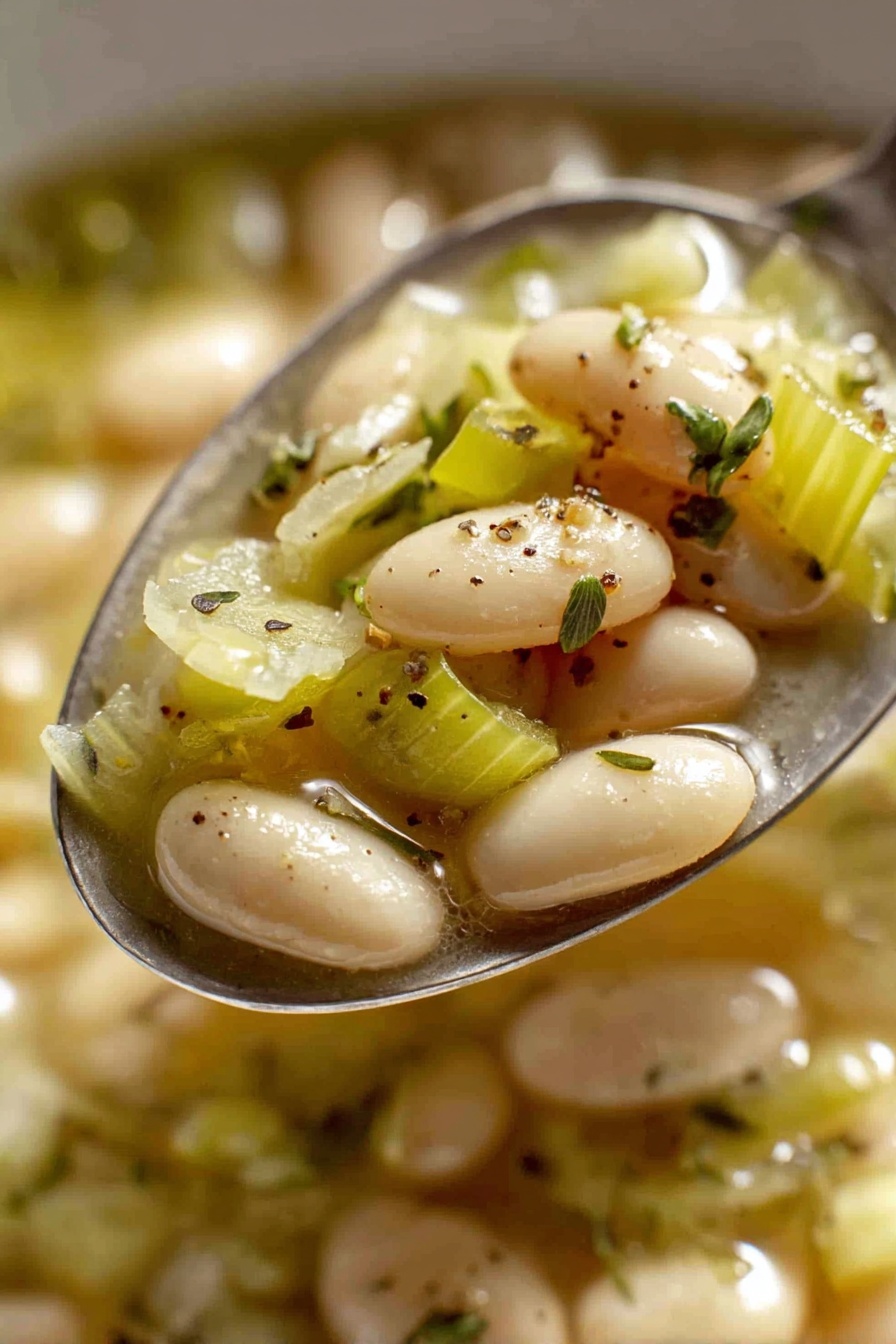Creamy Butter Bean and Leek, butter bean and leek dish, vegetarian creamy recipe, easy butter bean recipe, cozy leek and bean meal - The image shows a close-up view of a red pot filled with a warm soup made of white beans and chopped green cabbage pieces in a light broth. The beans are smooth and oval-shaped, scattered evenly throughout the soup, while the cabbage is soft and lightly translucent with a pale green color. Small specks of black pepper and fresh thyme sprigs are sprinkled on top for garnish. The pot has a shiny red exterior with a white interior and two handles on the sides. The pot is sitting on a white marbled surface. Photo taken with an iphone --ar 2:3 --v 7