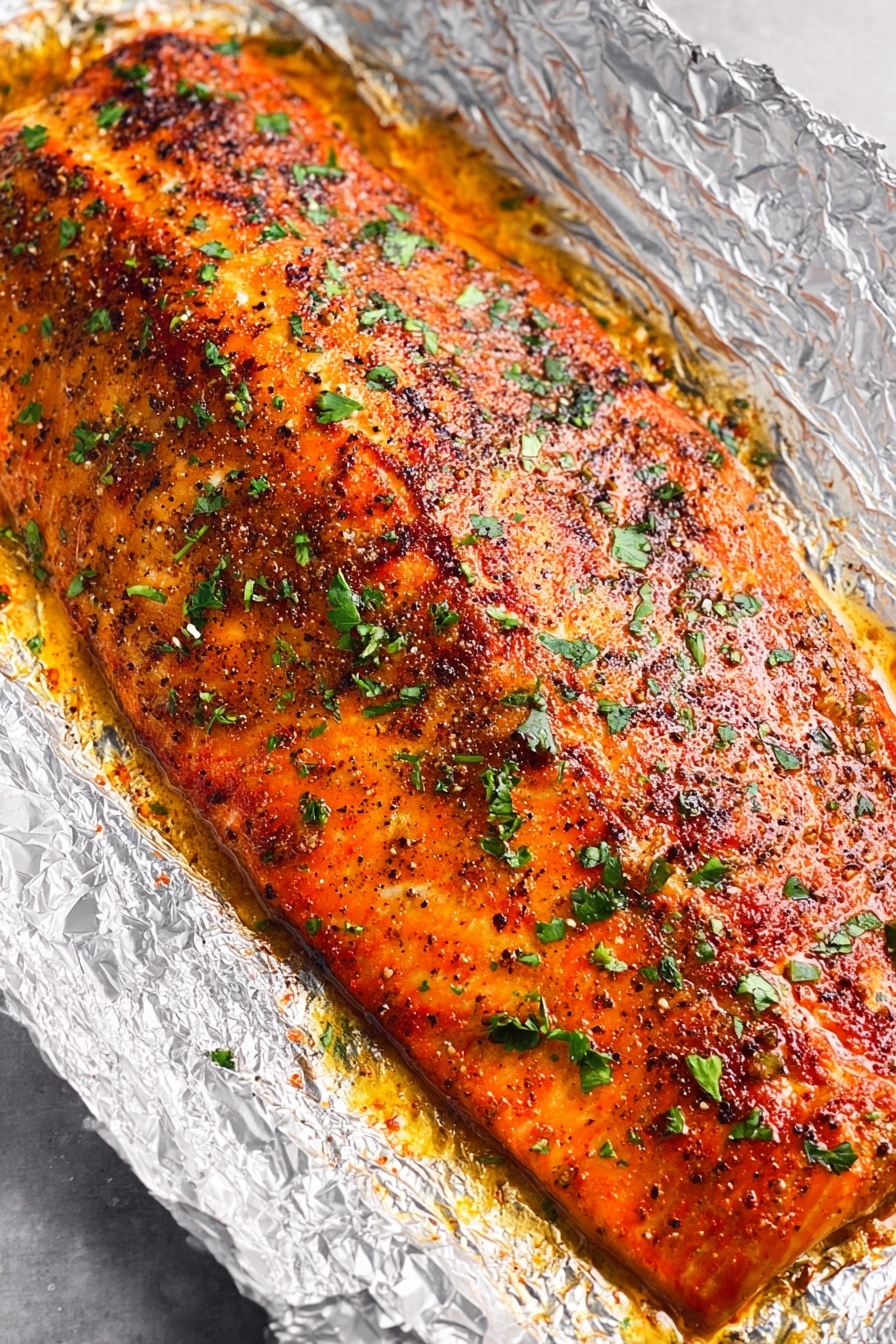 Oven Baked Salmon with Garlic Butter, baked salmon recipes, easy salmon dinner, healthy salmon fillet, flavorful salmon recipes - A large piece of cooked salmon lies on crinkled aluminum foil in a baking pan, with a golden-brown seasoned crust on top sprinkled with green herbs. The salmon is flaked in the lower right area, showing moist, soft, pink layers inside with some parts breaking apart. A silver fork rests next to the flaked salmon on the right side. The baking pan sits on a white marbled surface. photo taken with an iphone --ar 2:3 --v 7