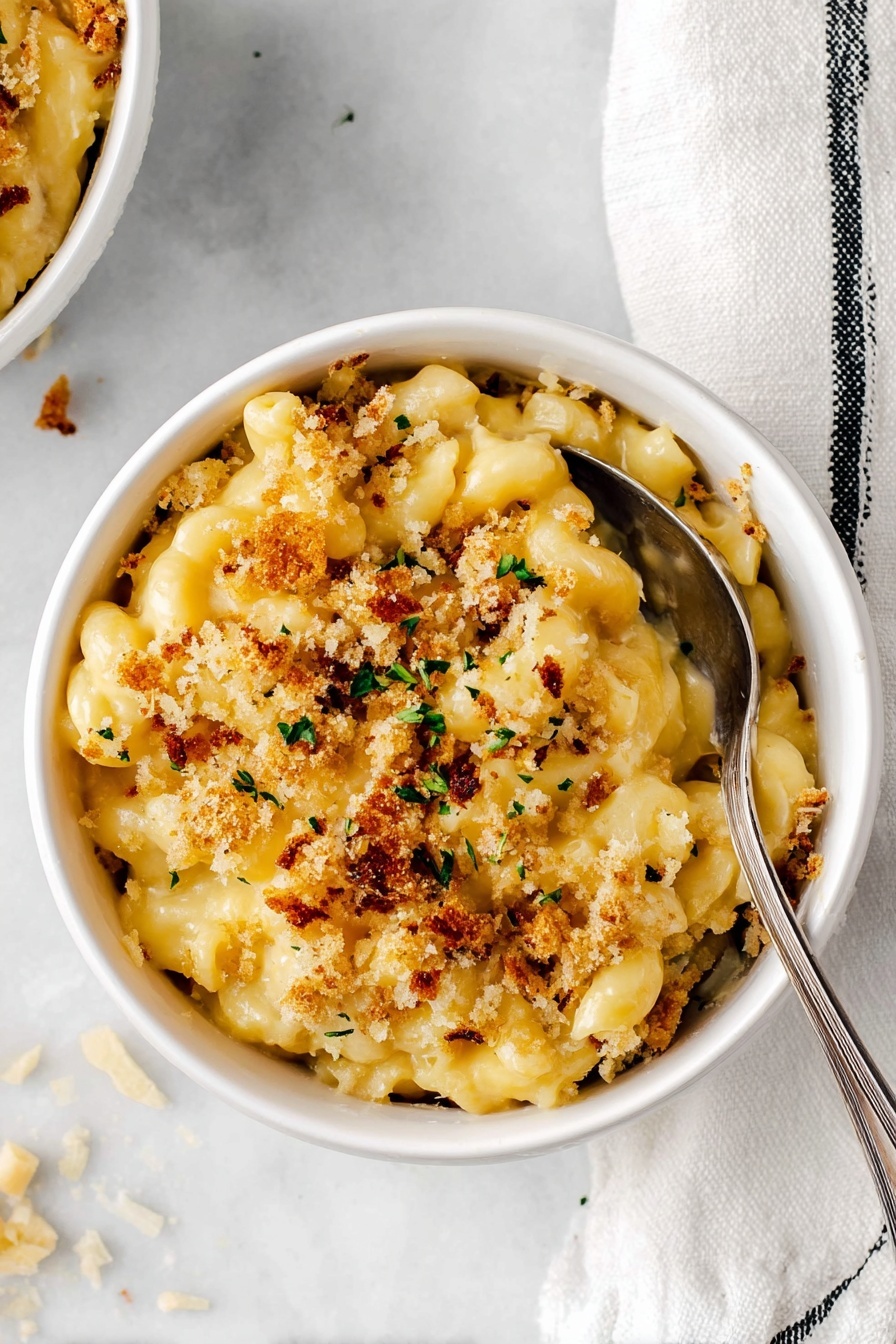 Baked Mac and Cheese with Pretzel Topping, cheesy baked mac and cheese, crunchy pretzel topping recipe, comfort food with a twist, gourmet mac and cheese - A white ceramic casserole dish holds a creamy macaroni and cheese bake with two main layers visible: the bottom thick layer of smooth, pale yellow macaroni pasta coated in rich cheese sauce, and the top layer of golden-brown crispy breadcrumb topping with small green specks sprinkled throughout. A wooden spoon lifts a generous scoop from the dish, showing the creamy macaroni stretching slightly below the crusty layer. The dish sits on a white marbled surface with a clean, bright background. Photo taken with an iphone --ar 2:3 --v 7