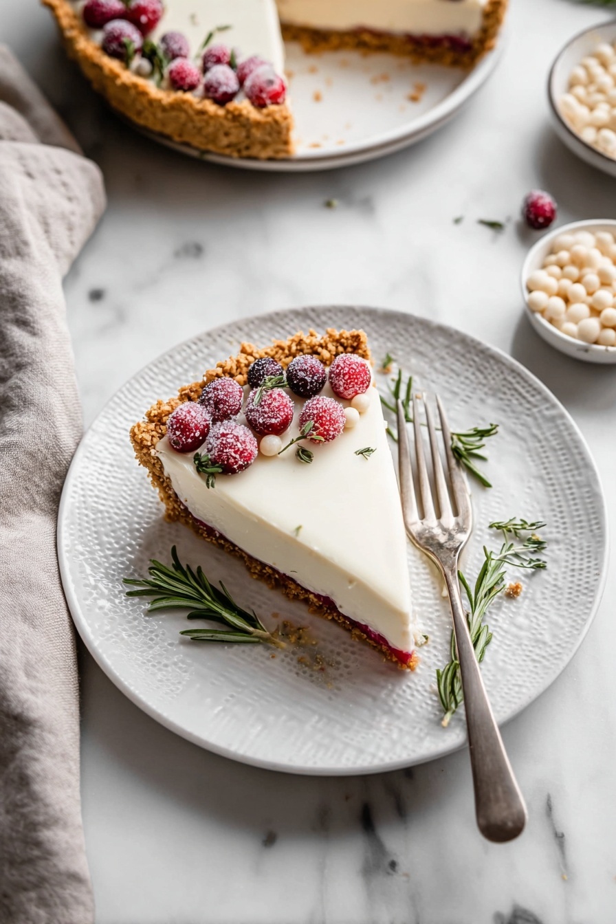 Cranberry White Chocolate Tart, festive dessert recipes, holiday tart ideas, easy tart recipes, rich dessert with cranberries and white chocolate - The image shows a slice of pie on a white plate with a textured rim, placed on a white marbled surface. The pie has three visible layers: a golden brown crumbly crust, a thin red layer in the middle, and a thick, smooth white topping. The slice is decorated on one side with sugared red cranberries, a few small white drops, and sprigs of fresh green rosemary. A silver fork rests on the right side of the plate. Nearby, there is a whole pie with a similar topping and decoration, and a bowl filled with small white drops. A light gray cloth is placed towards the bottom left corner of the image. Photo taken with an iphone --ar 2:3 --v 7