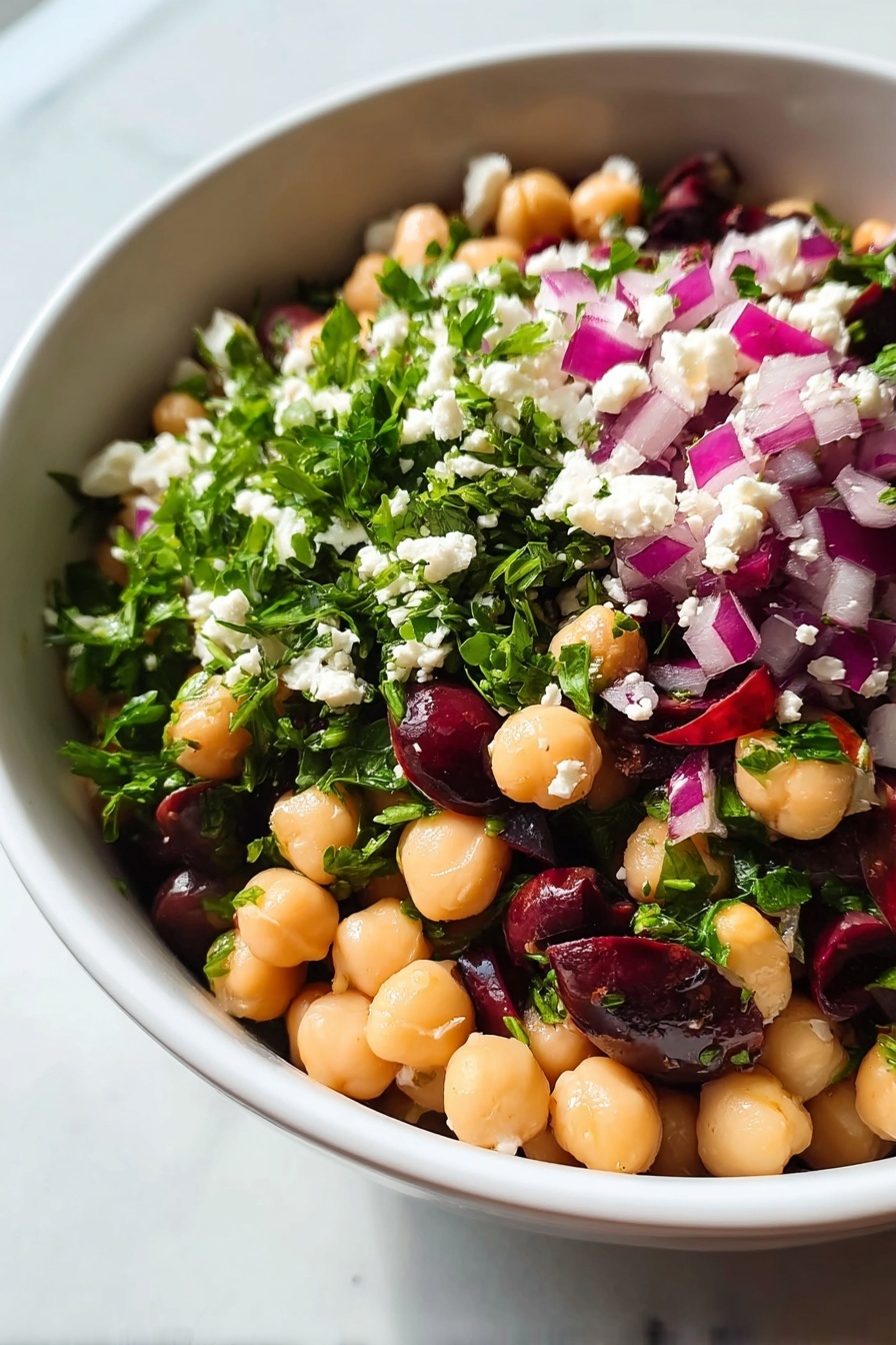 Chickpea and Black Bean Salad, Chickpea and Black Bean Salad Easy, Healthy Chickpea and Black Bean Salad, Vegetarian Bean Salad, Quick Vegetable Salad - A close-up view of a white bowl filled with a colorful chickpea salad, showing roughly three layers. The bottom layer consists of smooth, round pale beige chickpeas mixed with dark purple olives. The middle layer has bright green chopped leaves, likely parsley, scattered throughout. The top layer is dotted with small white cheese crumbles and chopped purple-red onions, adding texture and vibrant color contrast. The bowl sits on a white marbled surface. photo taken with an iphone --ar 2:3 --v 7