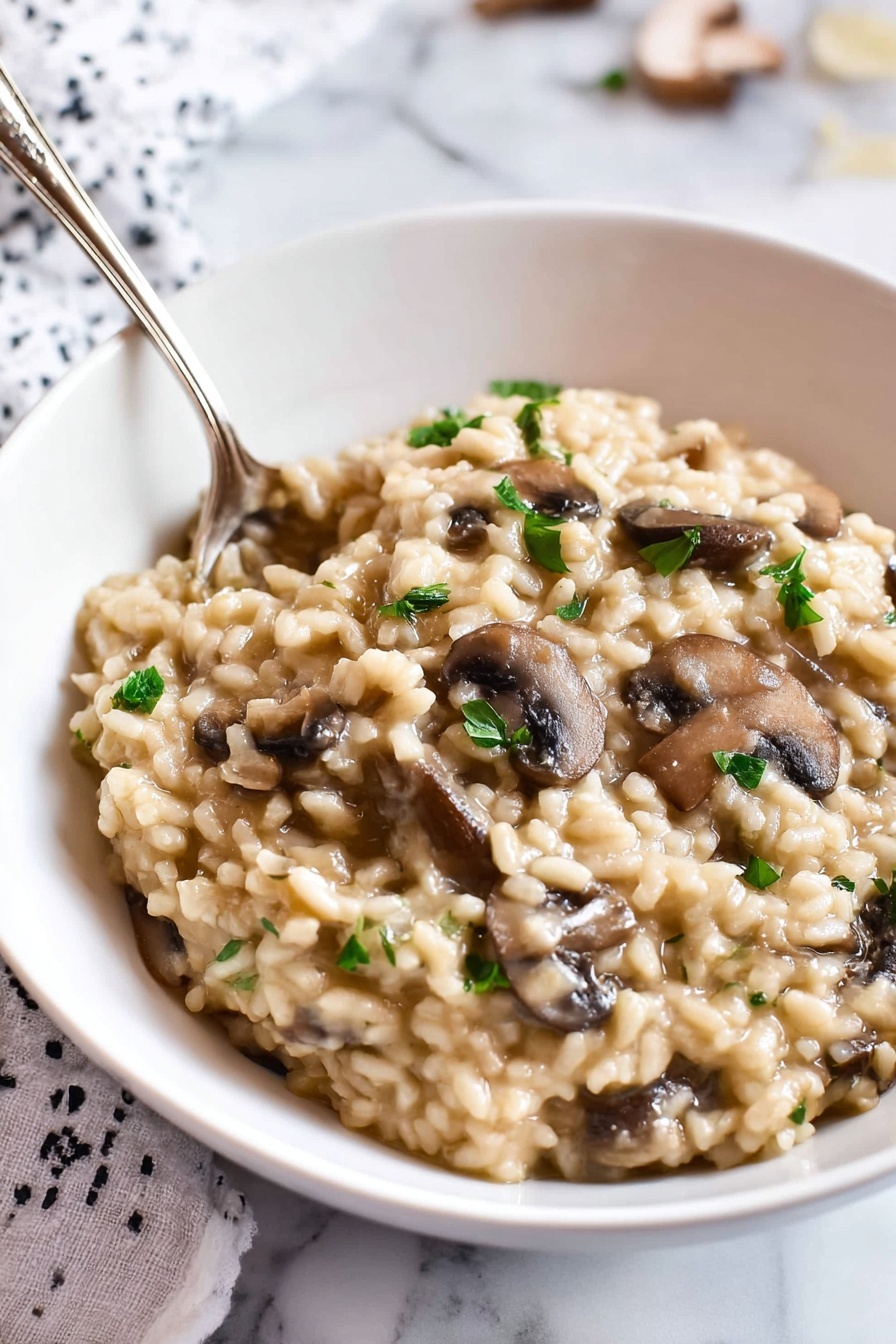 Pressure Cooker Mushroom Risotto, Mushroom Risotto Recipe, Easy Mushroom Risotto, Creamy Mushroom Risotto, Pressure Cooker Dinner - A white bowl filled with creamy mushroom risotto. The risotto has a thick, soft texture with plump, tender rice grains mixed with sliced brown mushrooms. Small pieces of green herbs are sprinkled on top, adding color contrast. A silver spoon is partially dipped into the risotto, resting near the edge of the bowl. The bowl sits on a white marbled surface with part of a white and black patterned cloth visible in the background. Photo taken with an iphone --ar 2:3 --v 7