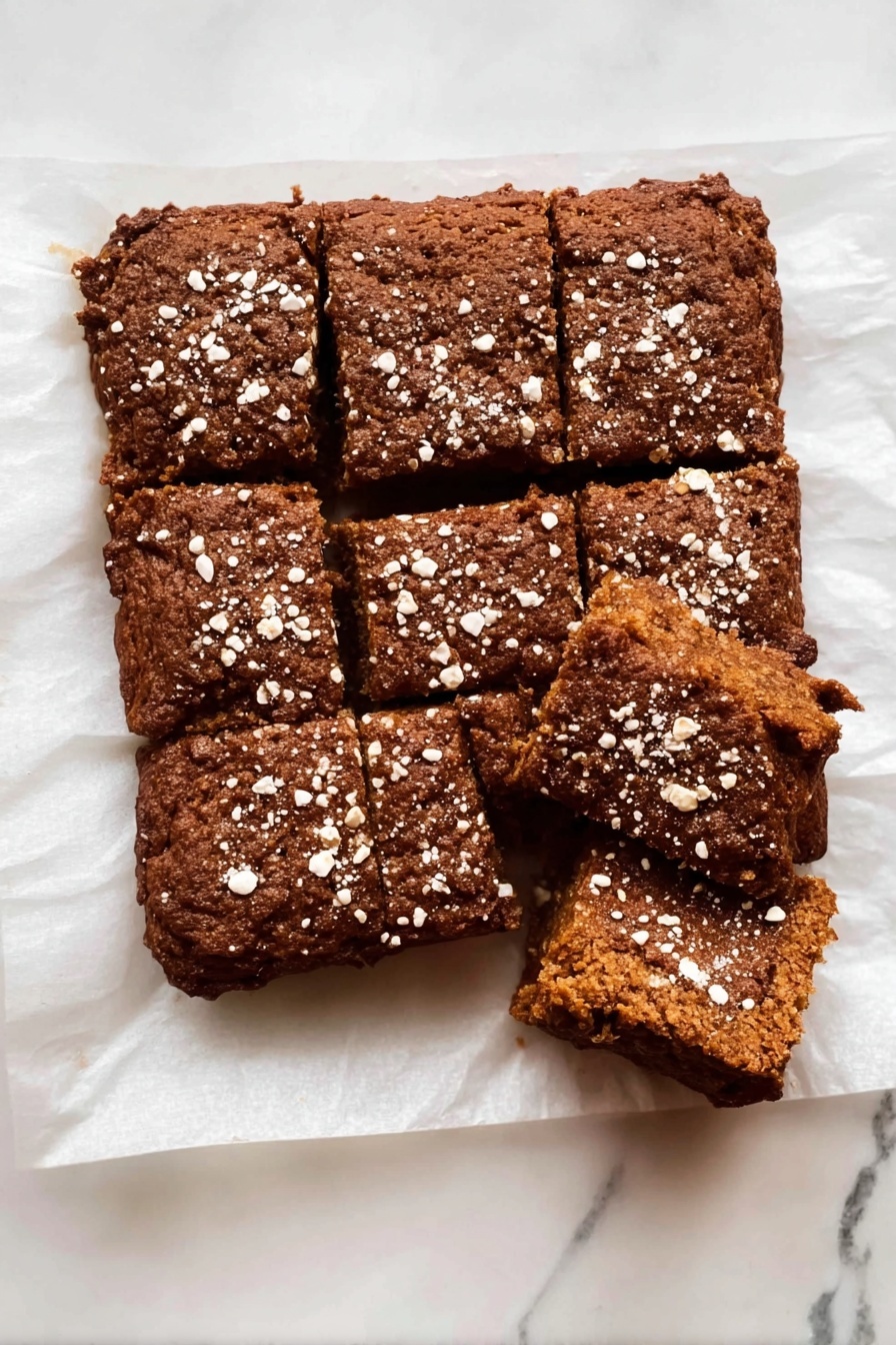 Healthy Apple Oatmeal Cake, healthy apple oatmeal cake, wholesome apple cake, gluten-free oatmeal dessert, nutritious fruit breakfast - The dish is a rectangular brown baked cake cut into nine pieces with a rough texture and a slightly cracked top. The cake is sprinkled with white oat flakes spread unevenly over the surface. It rests on white parchment paper placed on a white marbled surface. One piece in the top right corner is separated from the rest, showing the inside of the cake, which is soft and dense with a uniform brown color. photo taken with an iphone --ar 2:3 --v 7