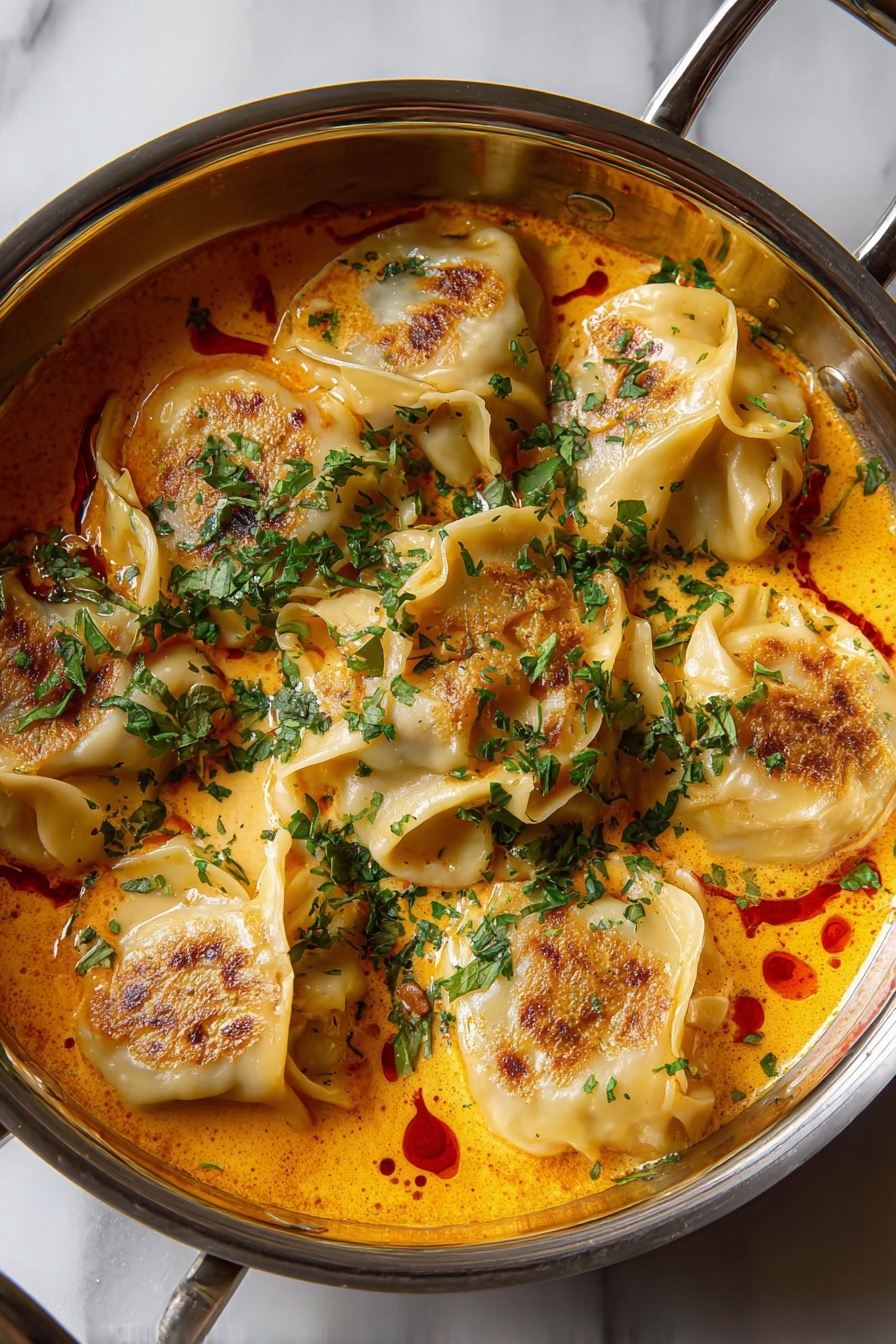 Vegan Coconut Curry Soup with Dumplings, vegan Thai curry soup, coconut curry soup recipe, vegan dumpling soup, plant-based coconut curry - A shiny metal pan contains seven dumplings that are layered in a creamy orange sauce. The dumplings have a light beige color with some browned spots on top, showing slight crisp edges. The orange sauce has a smooth texture with small red oil droplets scattered across the surface. Fresh, chopped green herbs are sprinkled generously over the dumplings and sauce, providing a bright contrast. The pan is placed on a white marbled surface. Photo taken with an iphone --ar 2:3 --v 7