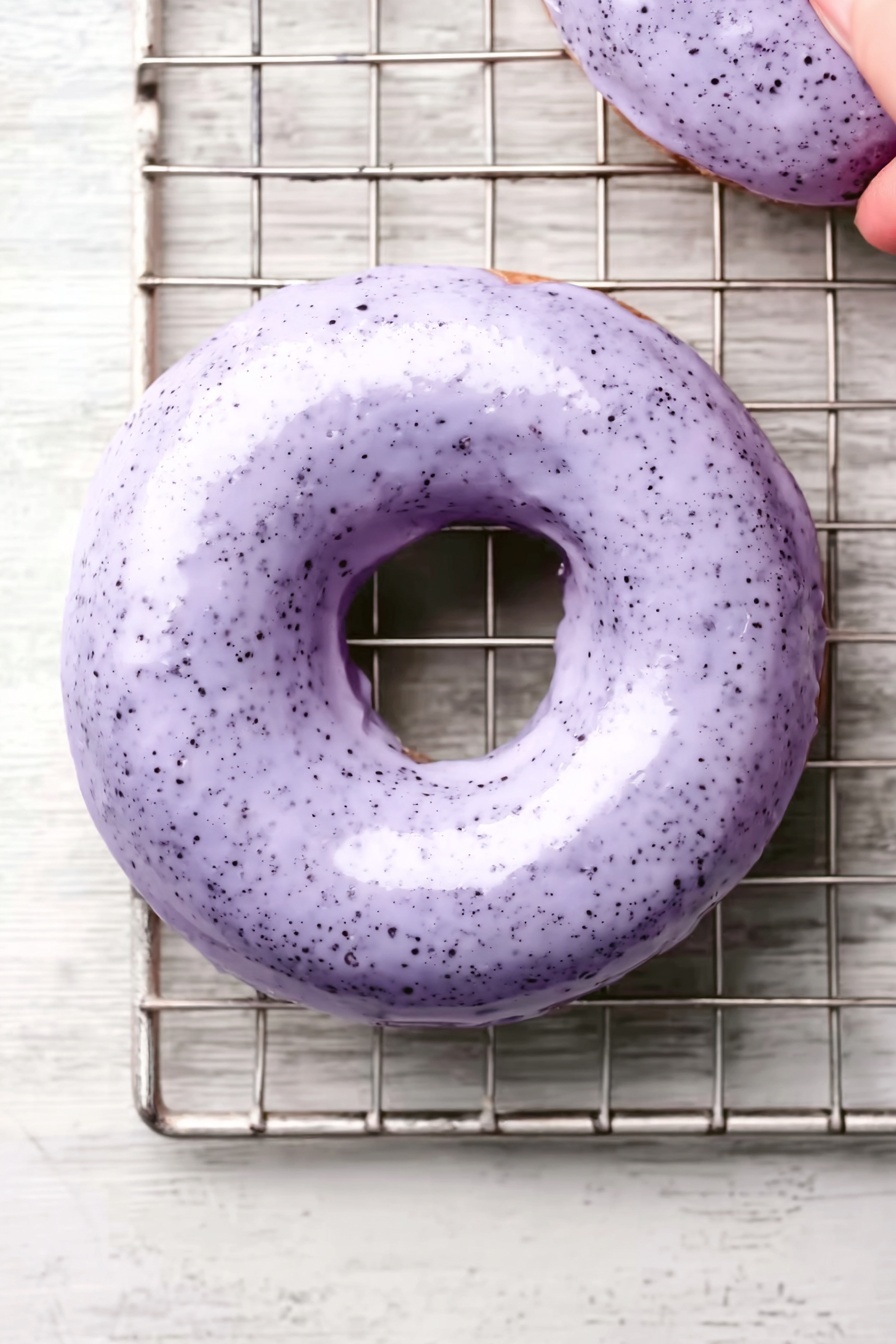 Wild Blueberry Cake Donuts, blueberry baked donuts, wild blueberry dessert, easy blueberry donut recipe, blueberry glaze donuts - Six donuts are on a round wooden board placed on white marbled texture. Each donut has a thick, smooth light purple glaze that looks creamy with tiny darker purple spots. The glaze covers the top and drips slightly over the sides, with some uneven edges. The donuts themselves are a bit visible under the glaze and seem to be light brown or greenish. The light shows soft reflections on the glaze, making it look fresh and shiny. Photo taken with an iphone --ar 2:3 --v 7