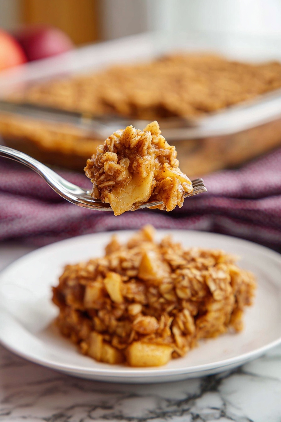 Apple Cinnamon Baked Oatmeal, healthy breakfast oatmeal, cozy breakfast ideas, easy baked oatmeal recipe, wholesome apple cinnamon oats - A single square piece of oat crumble dessert sits in the center of a white plate with ridged edges. The dessert has two main layers: the top layer is golden brown with a rough texture made of baked oats mixed with cinnamon, while the bottom layer appears softer and darker, showing a moist filling beneath the oats. The plate is placed on a wooden table, and in the background, there is a glass baking dish with more of the same oat crumble. A dark red and white checkered cloth is also slightly visible behind the plate. Photo taken with an iphone --ar 2:3 --v 7