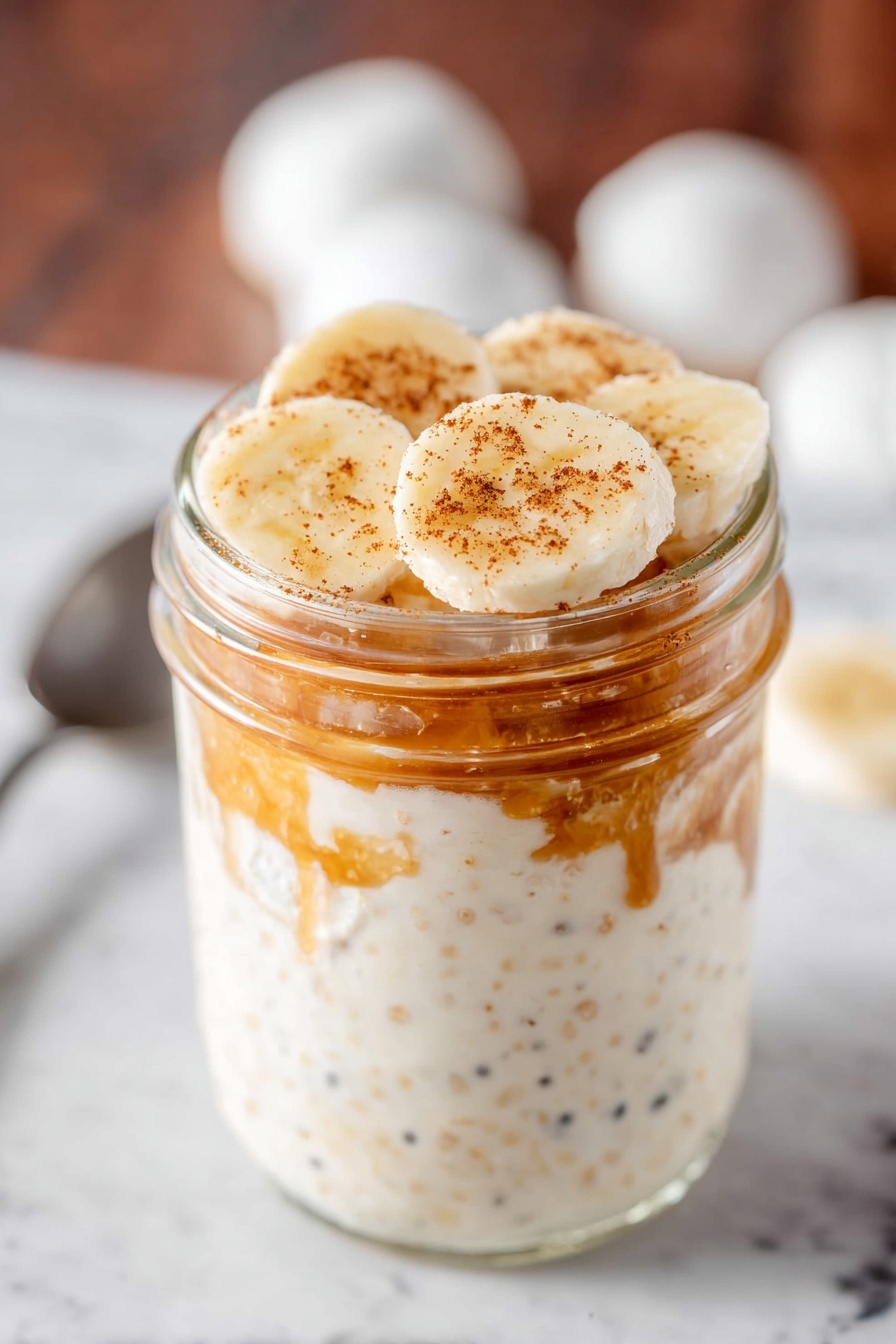 Peanut Butter Banana Overnight Oats, healthy overnight oats with peanut butter, quick breakfast ideas, banana oats recipe, nutritious breakfast recipes - A clear glass jar with a silver metal lid filled with three layers of overnight oats. The bottom layer is creamy white with tiny pieces of oats and seeds showing through. The middle layer has a light brown chunk inside the creamy oats mixture creating a rough texture. The top layer blends smoothly into the silver lid. The jar sits on a white marbled surface with scattered oats around, a white cloth on the left, and a yellow banana on the right photo taken with an iphone --ar 2:3 --v 7