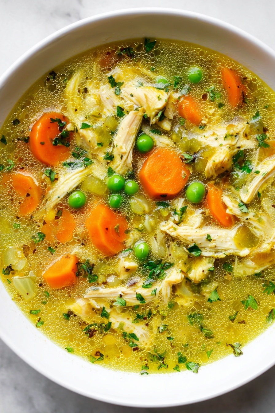 Turmeric Chicken Soup with Coconut Milk, healthy turmeric chicken soup, nourishing coconut milk soup, comforting spicy chicken soup, easy turmeric soup recipe - A close-up view of a white bowl filled with chicken soup. The soup has many layers: on top are bright orange carrot slices, green peas, and pale green celery pieces mixed with shredded light yellow chicken. The broth is clear with a yellow tint and small green herb bits floating throughout. There is a silver spoon resting in the soup, with a woman's hand holding the spoon near the edge of the bowl. The bowl is placed on a white marbled surface. Photo taken with an iphone --ar 2:3 --v 7