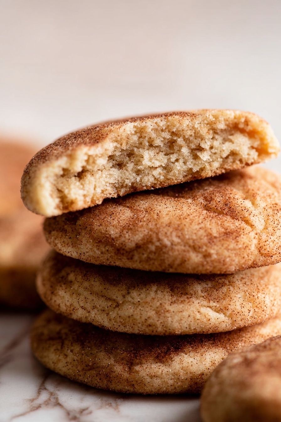 Brown Butter Snickerdoodle Cookies, cinnamon sugar cookies, buttery snickerdoodle recipe, soft cinnamon cookies, easy cookie recipes - A close-up shows a woman's hand holding a round cinnamon sugar cookie with a bite taken out of the top. The cookie has a golden-brown color with a visible coating of cinnamon sugar that gives a slightly rough texture. The woman's thumb has a yellow nail polish, and the plain white marbled background softly blurs behind the cookie, drawing attention to the details on the cookie's surface and the soft texture where it was bitten photo taken with an iphone --ar 2:3 --v 7